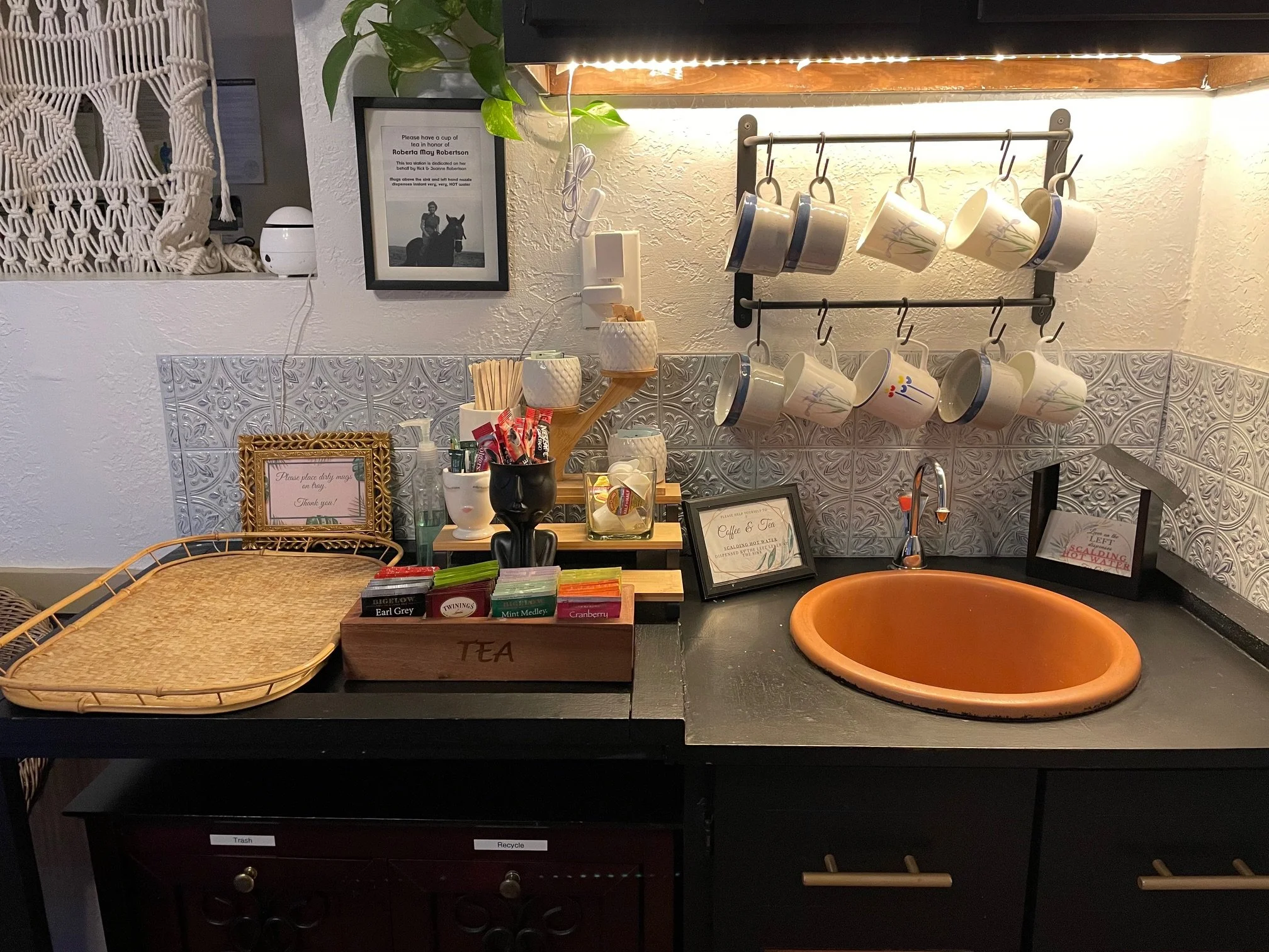 Photo of tea station with mugs hanging on a wall, a selection of tea and a sink