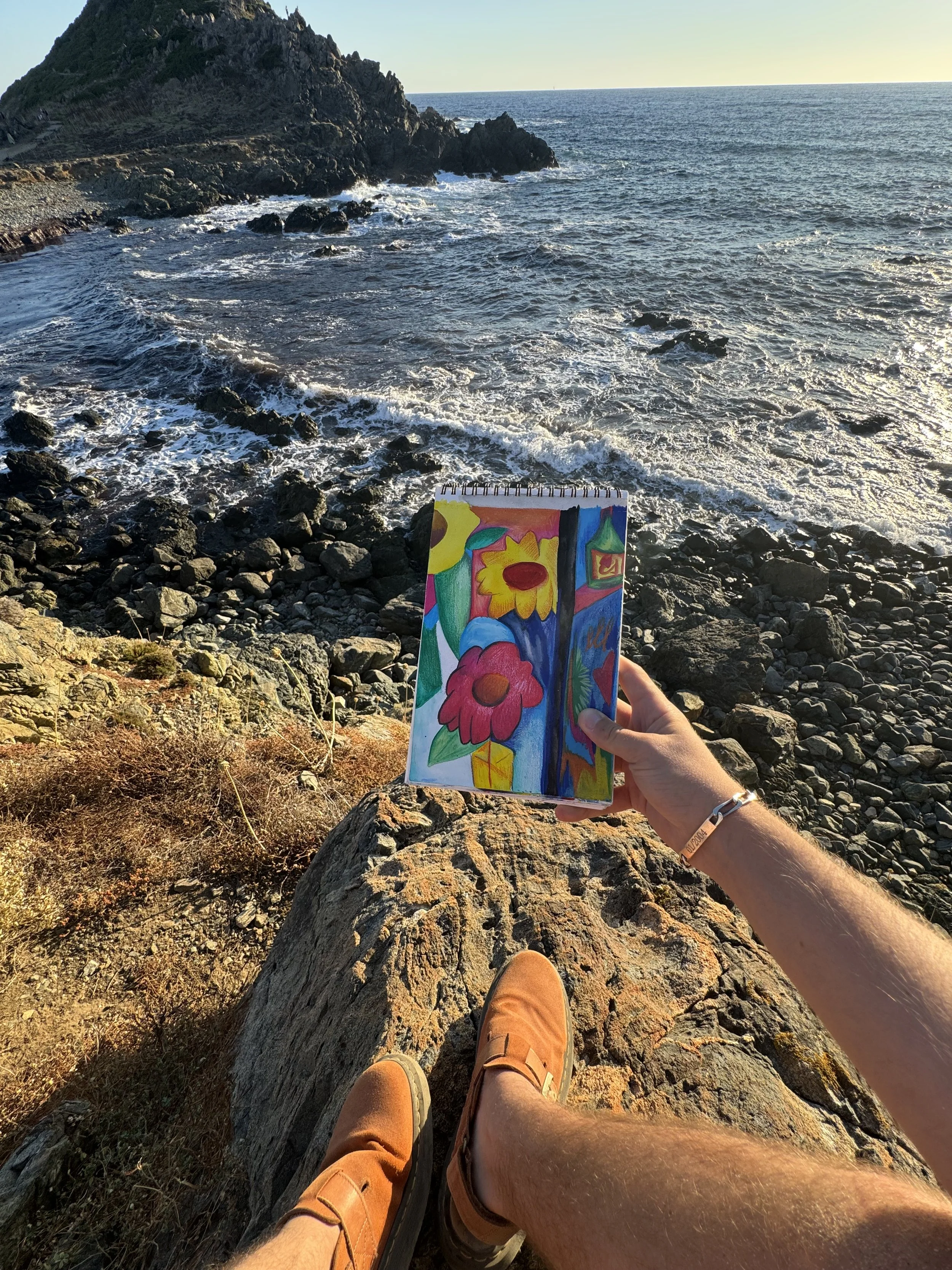 Œuvre contemporaine florale de Crown* présentée dans la main de l’artiste au bord de la mer