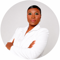 Portrait of an African American woman with short hair, wearing a white blazer, standing with arms crossed against a light gray background.