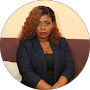 A woman with curly hair and glasses sitting with arms crossed in a professional environment.