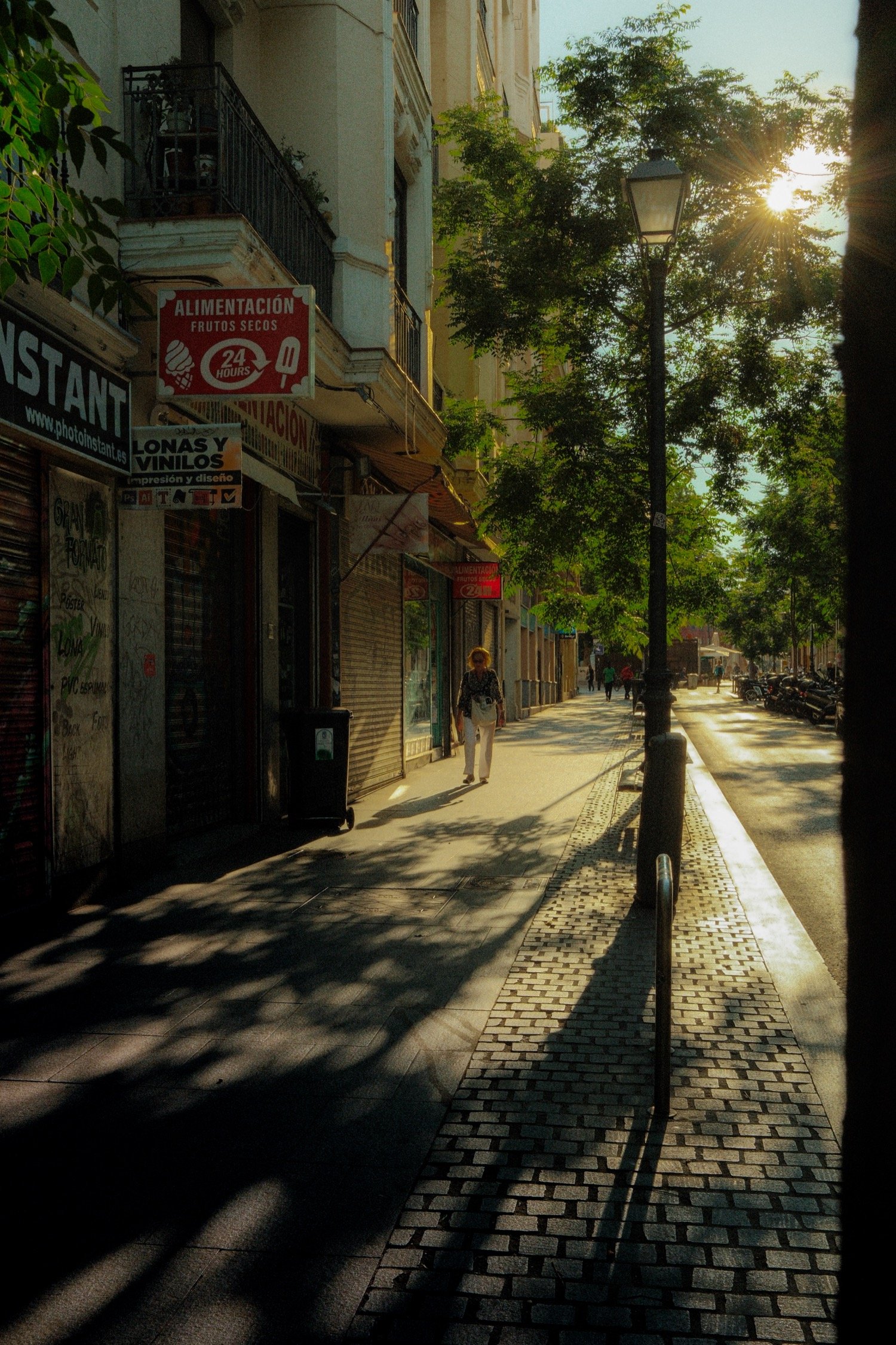 Early morning sunlight casting long shadows on a quiet Madrid street with a woman walking by storefronts