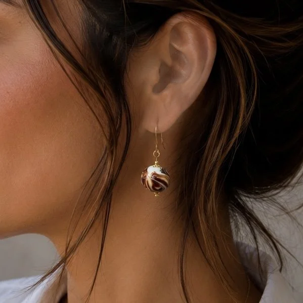 Mujer llevando pendientes Marble Rojo de vidrio de Murano artesanal y plata de ley chapada en oro con elegante efecto marmolado.