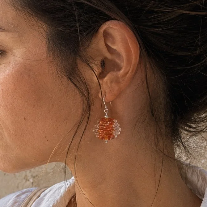 Mujer llevando pendientes Luar Ámbar de vidrio de Murano artesanal y plata de ley con reflejos dorados y cálidos.