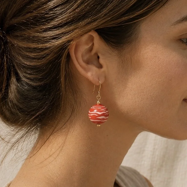 Mujer llevando pendientes Coralina de vidrio de Murano artesanal y plata de ley con reflejos cálidos y luminosos.