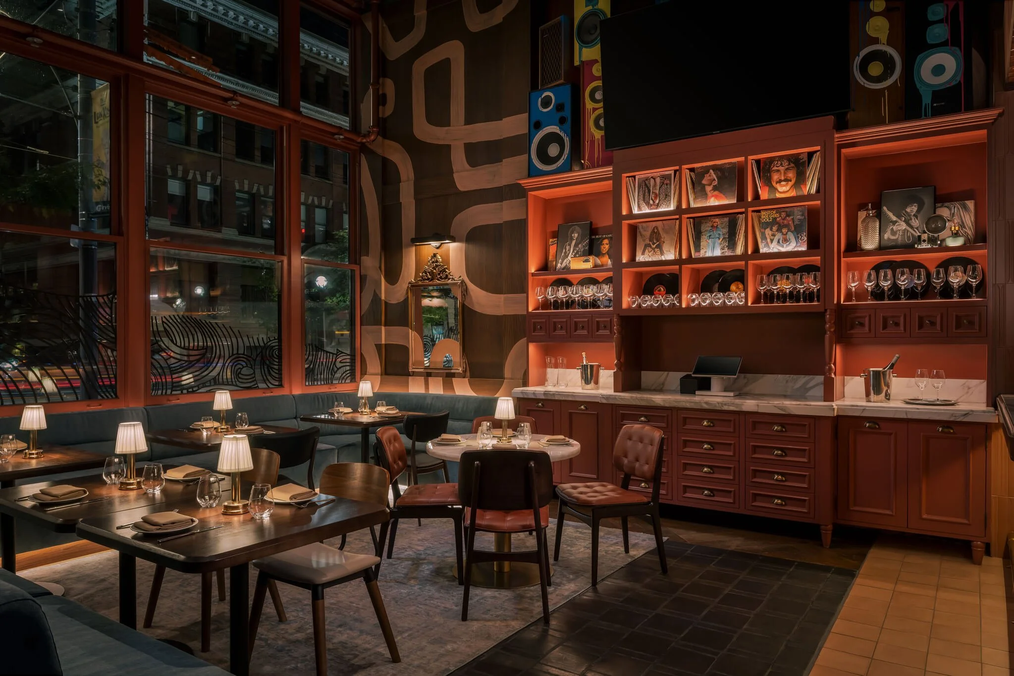 Interior of a cozy, dimly lit restaurant with wooden furniture, wine glasses, and artworks on the wall.