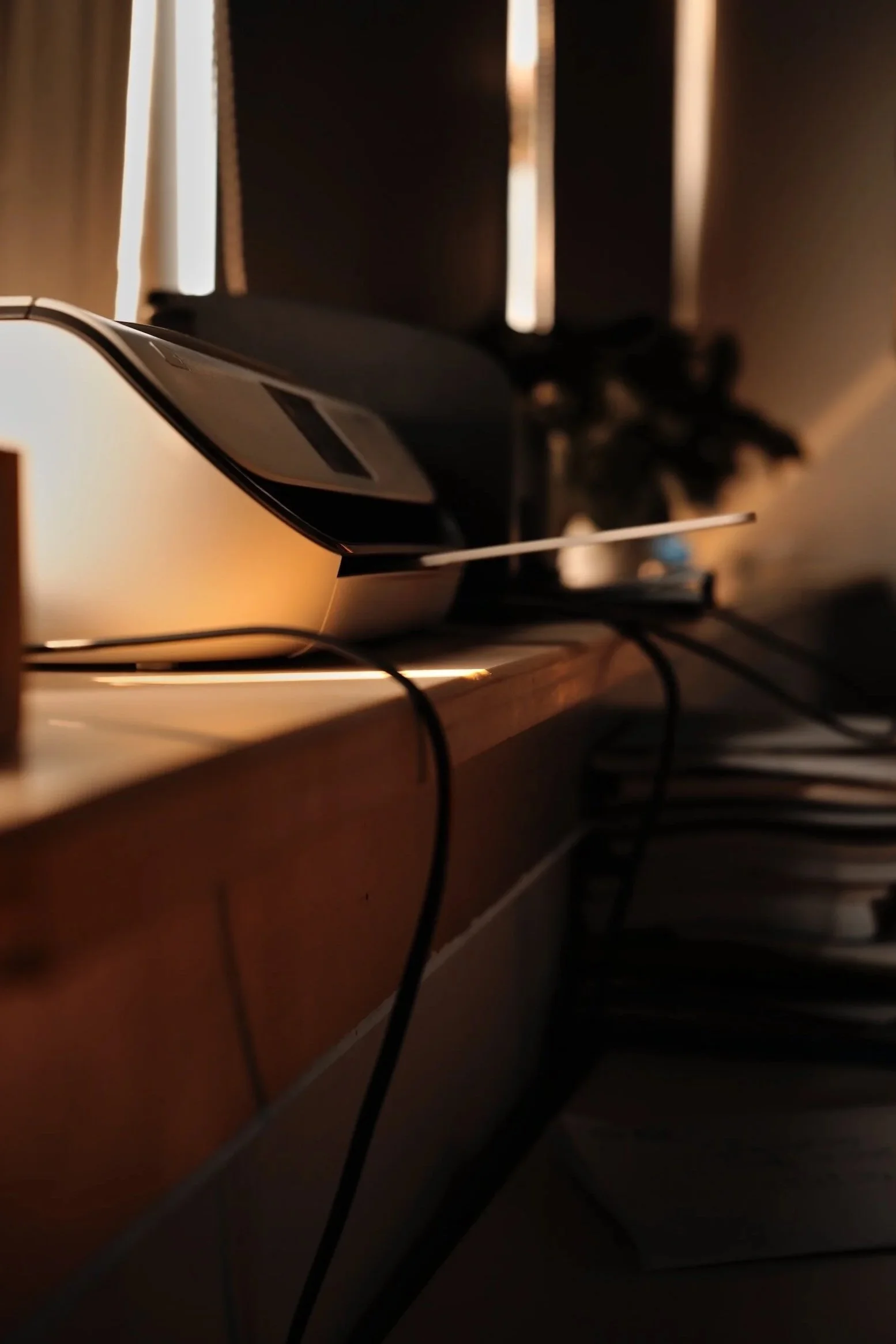 Close-up of a computer mouse on a desk, with a blurred background of dark curtains and light filtering through.