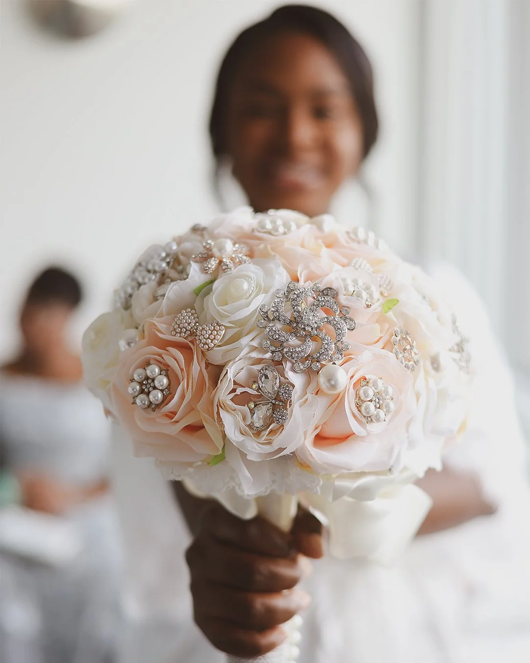 Woman holding a bouquet of pink and white roses decorated with pearl and rhinestone jewelry.