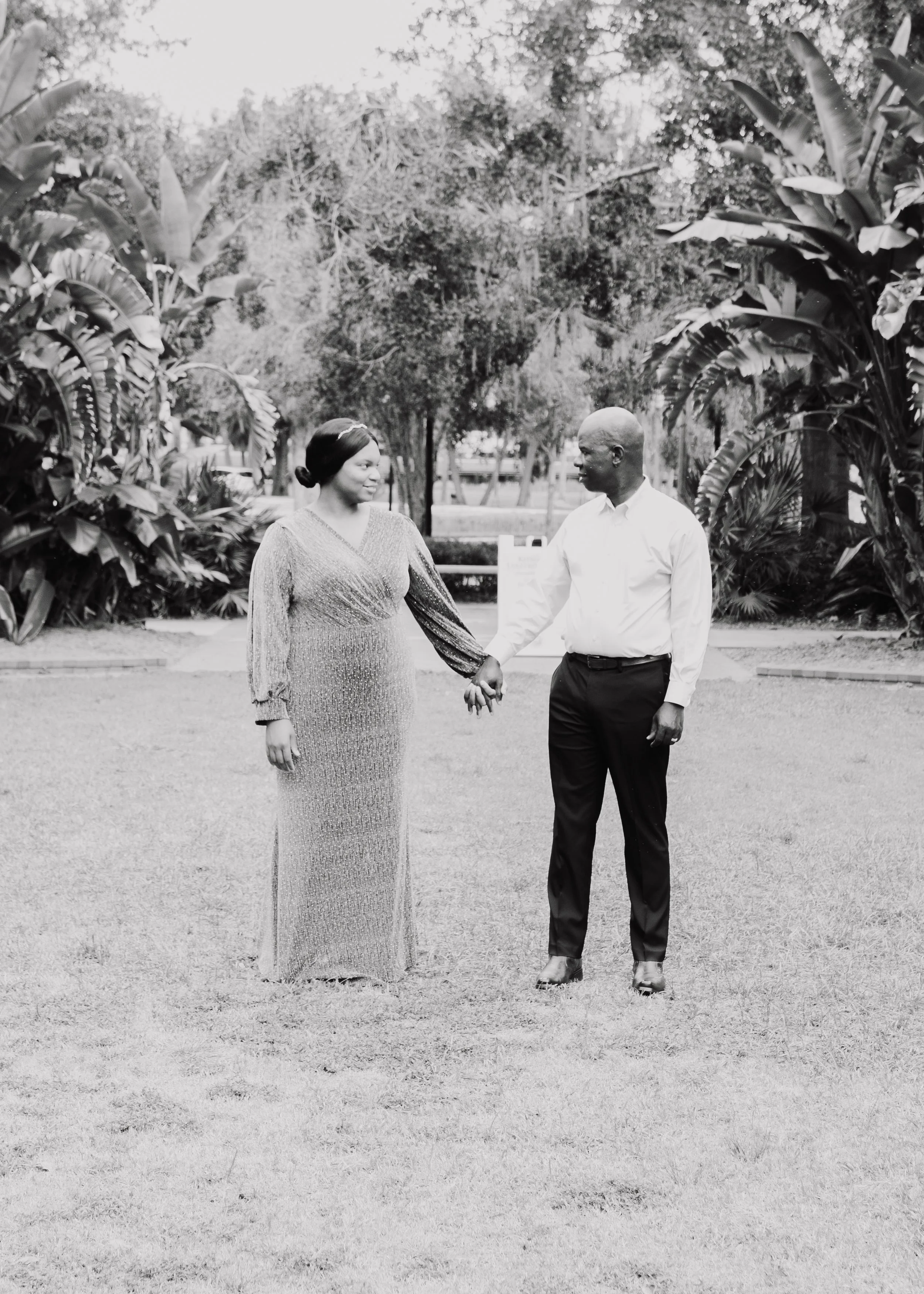 A couple holding hands outdoors in a park-like setting with trees and plants.