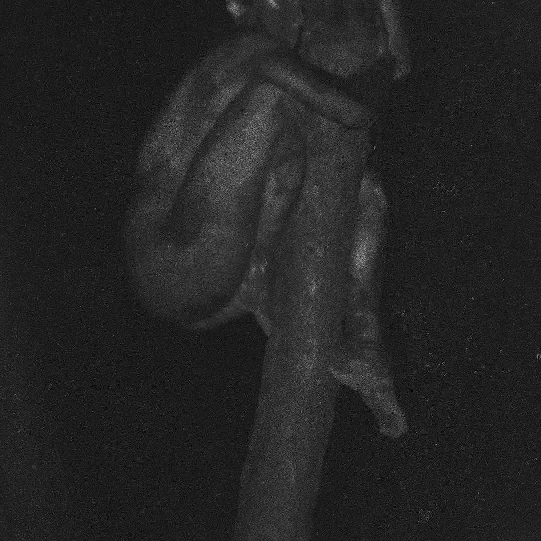 Dark-colored sculpture of a hand holding a small child, made of stone or similar material, viewed in dim lighting.