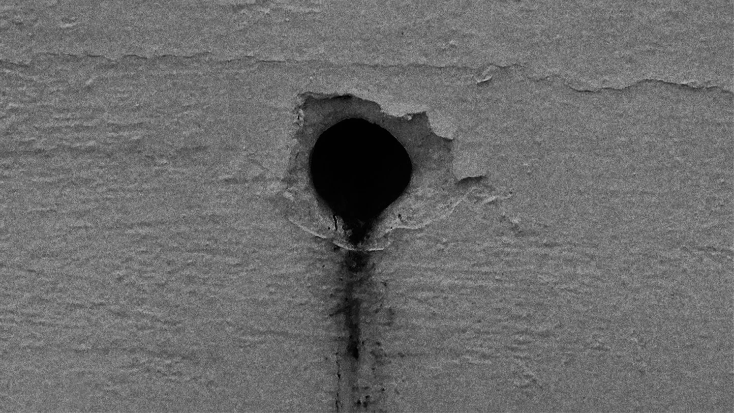 Close-up of a hole in a gray wall with a dark interior and paint streaks below it.
