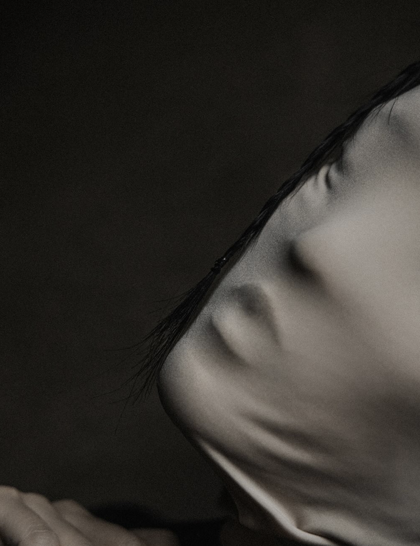 Close-up of a person's closed eye, nose, and lips in black-and-white, with hair falling across the face.