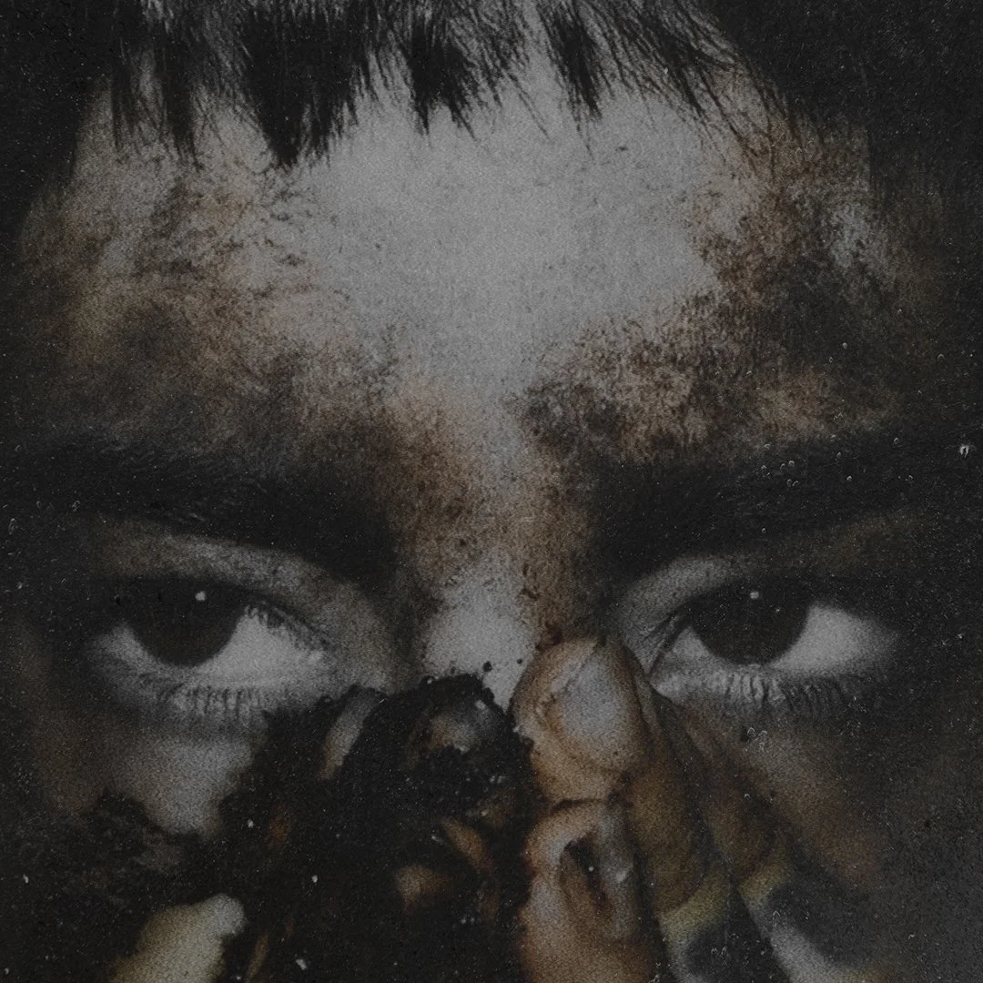 Close-up of a person's face with eyes visible and dark makeup, with brown paint or substance smeared over the nose and face, and black paint around the eyes.