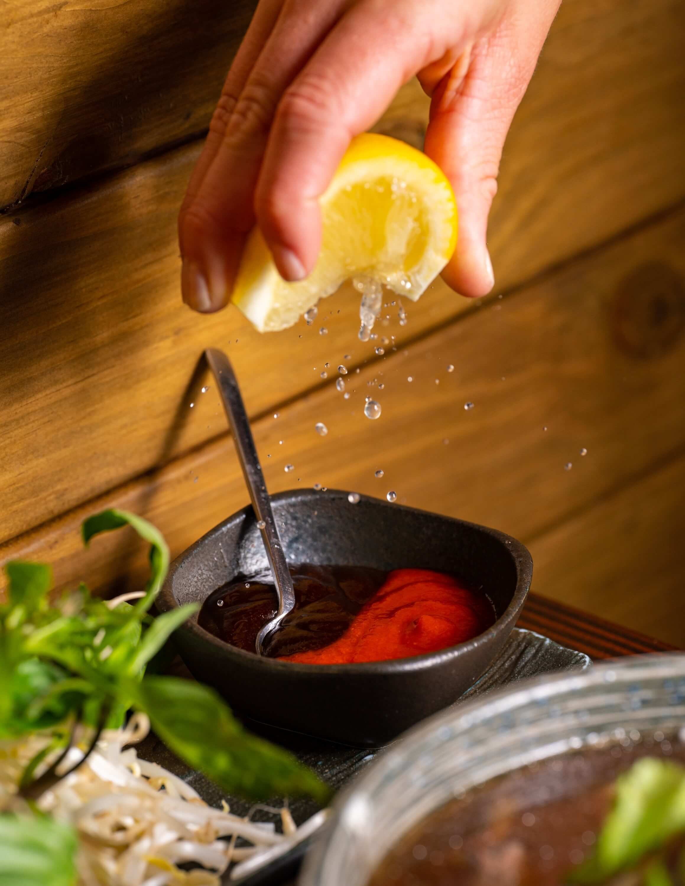  squeezing a slice of lemon into a dipping sauce 