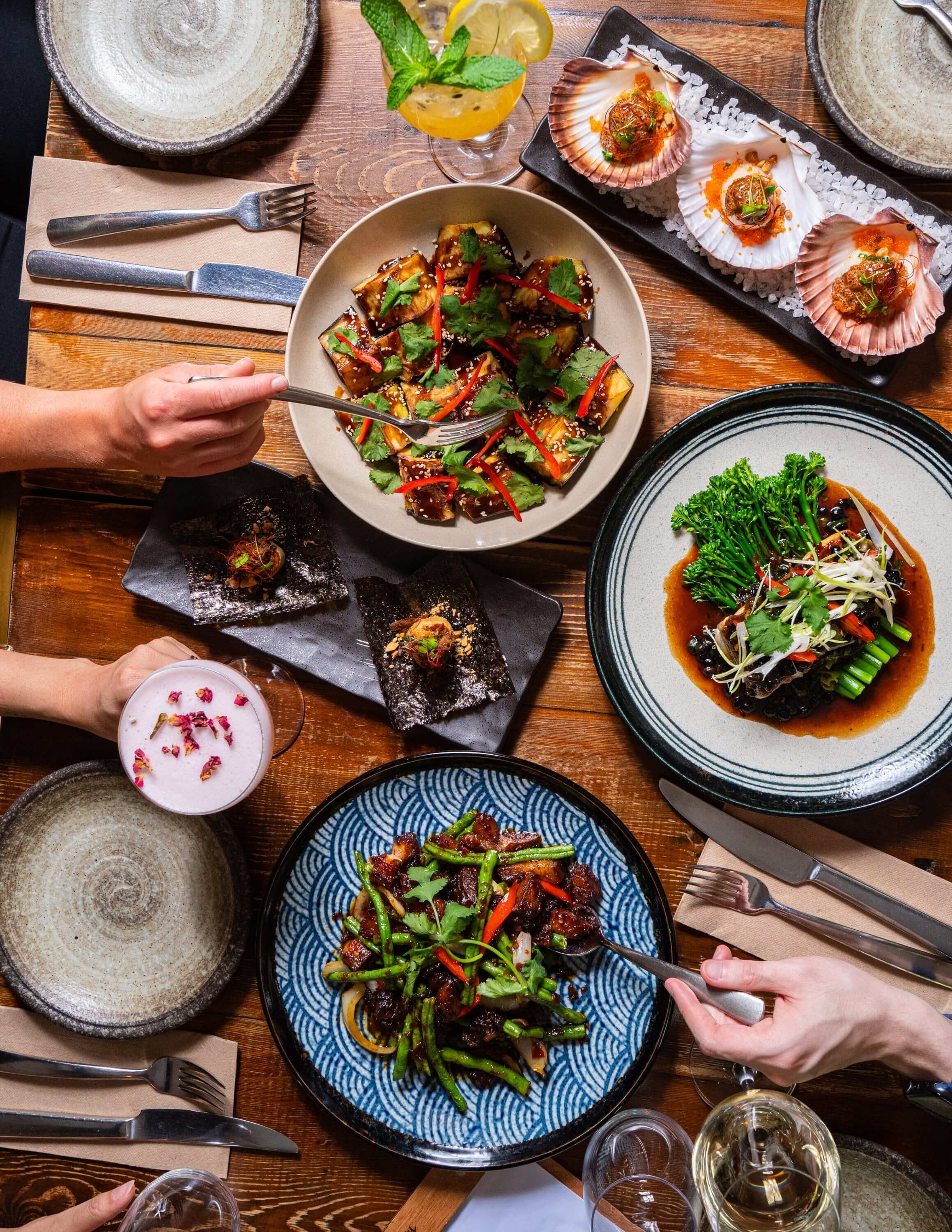  a lat lay image of hand passing food across a banquette of Vietnamese food 