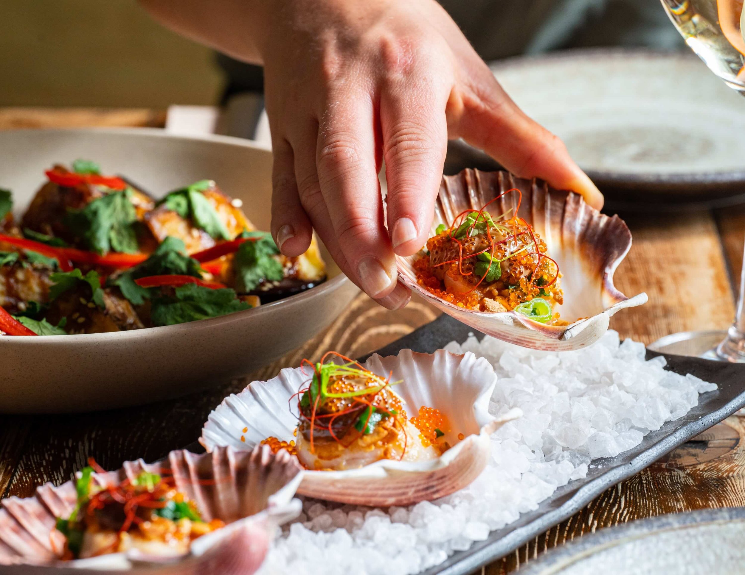  someone picking up a scallop in a shell with chilli and fresh herbs 