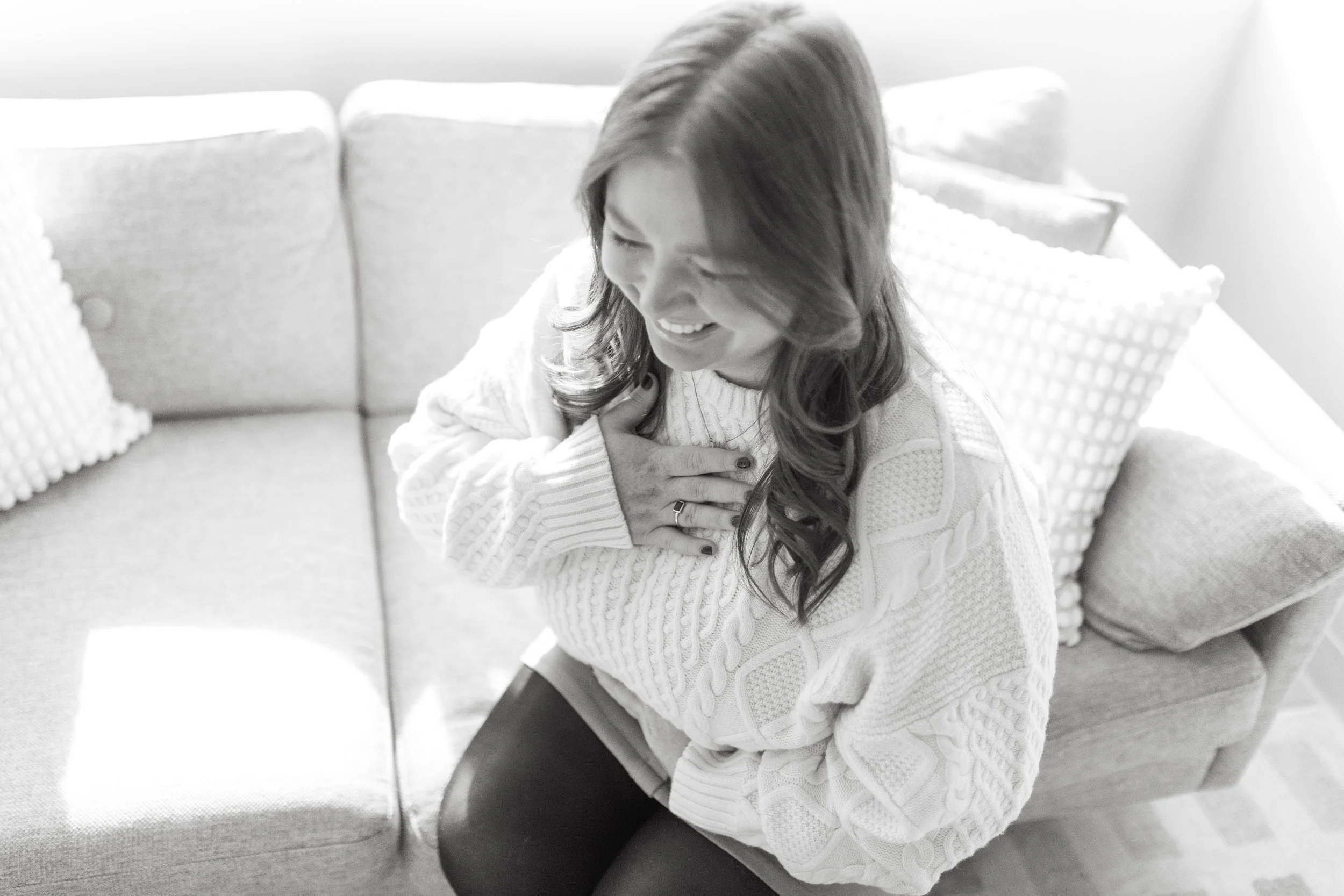 A woman sitting on a couch clutching her chest with an expression of pain or discomfort.