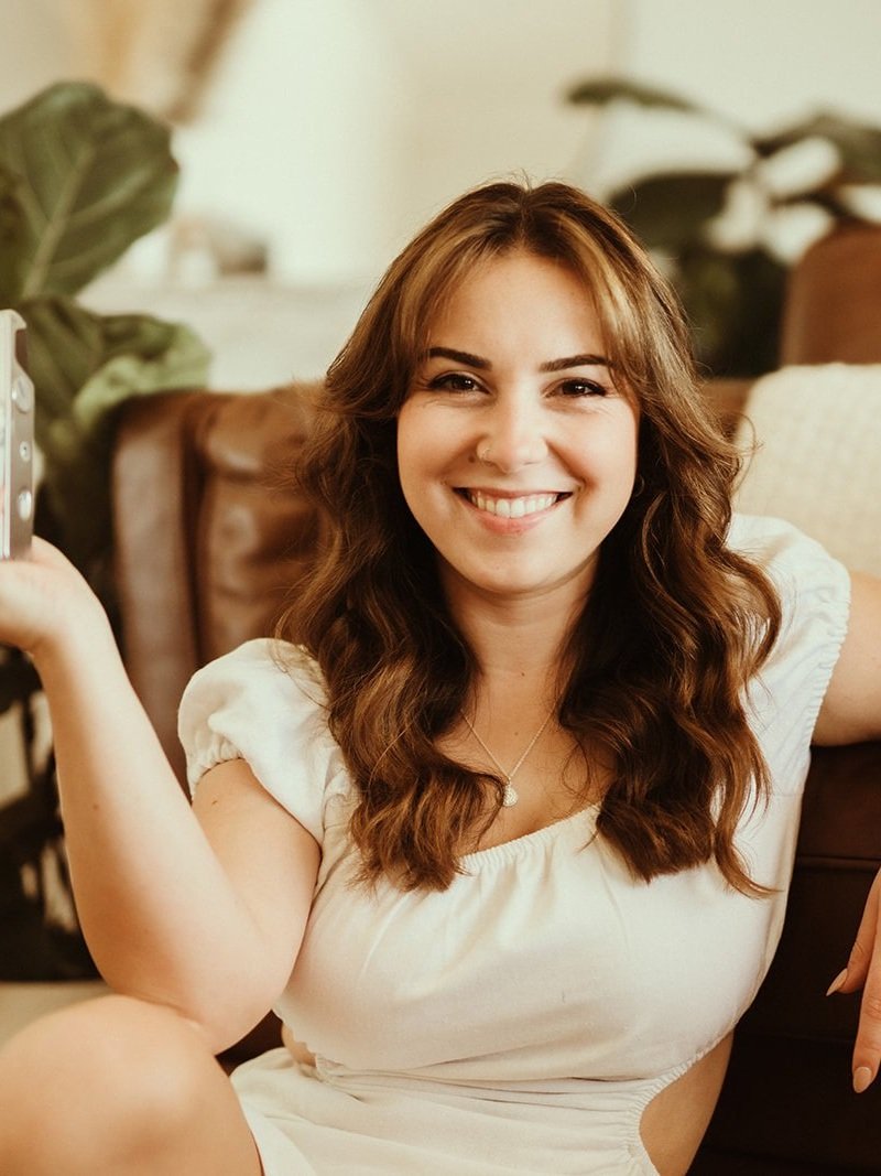 Designer and business owner, Kaitlyn, smiling front on at camera with old film camera.