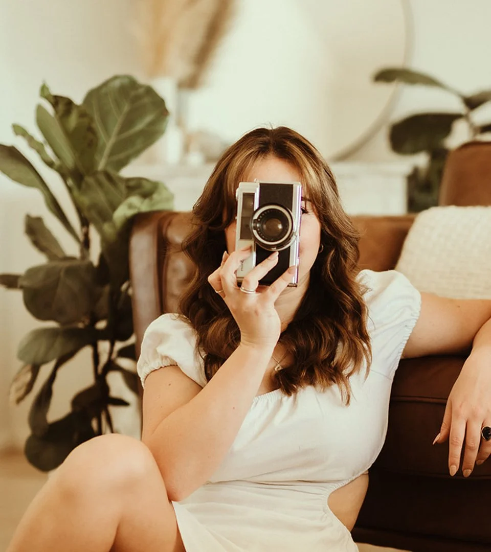Designer holding camera in front of face in white dress.jpg