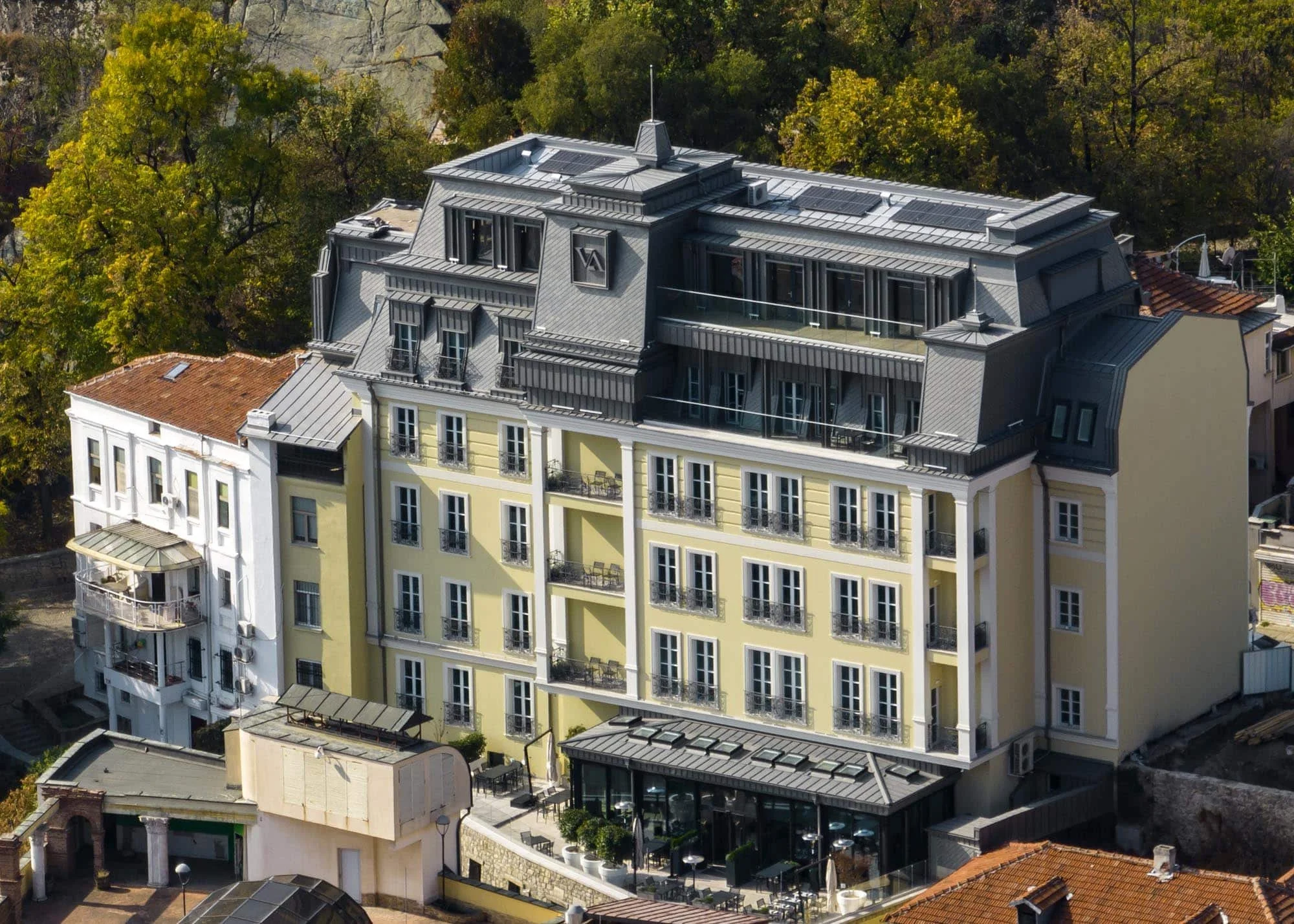 A multi-story yellow building with a gray roof and numerous windows, surrounded by trees.