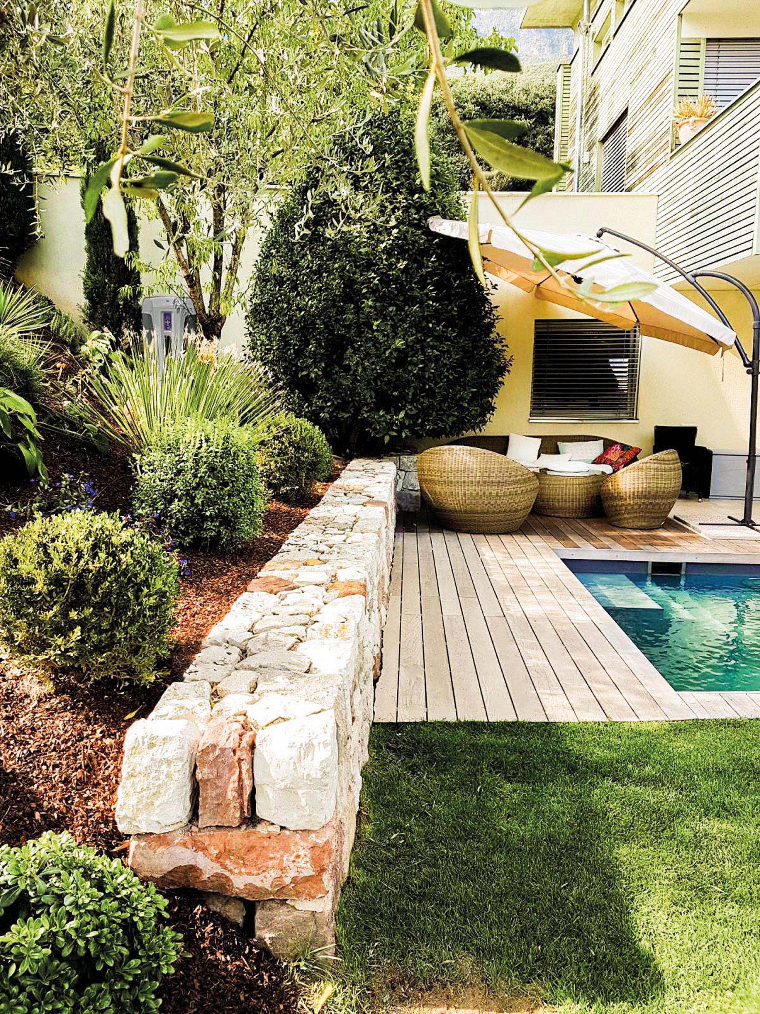 Garten mit Pool, Liegesessel, Sonnenschirm, viele grüne Pflanzen und Bäume, Ziersteine, Holzdielen und Rasenfläche