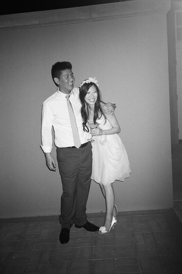 A man and woman at a formal event, standing close, both smiling, the woman holding a glass, the man with his arm around her.