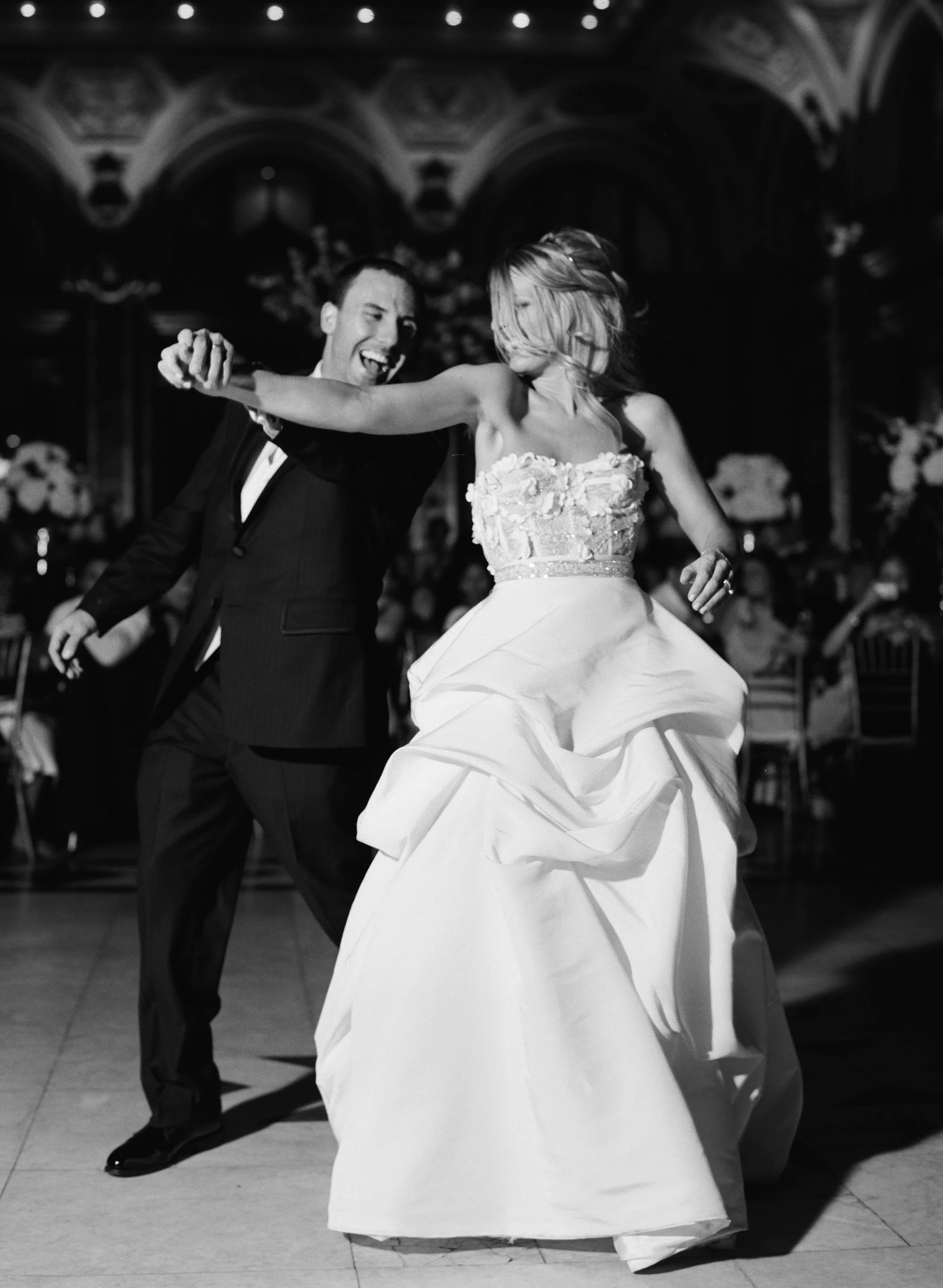 A man and woman dancing at a wedding reception, with the woman in a wedding dress and the man in a suit, in a decorated indoor venue.