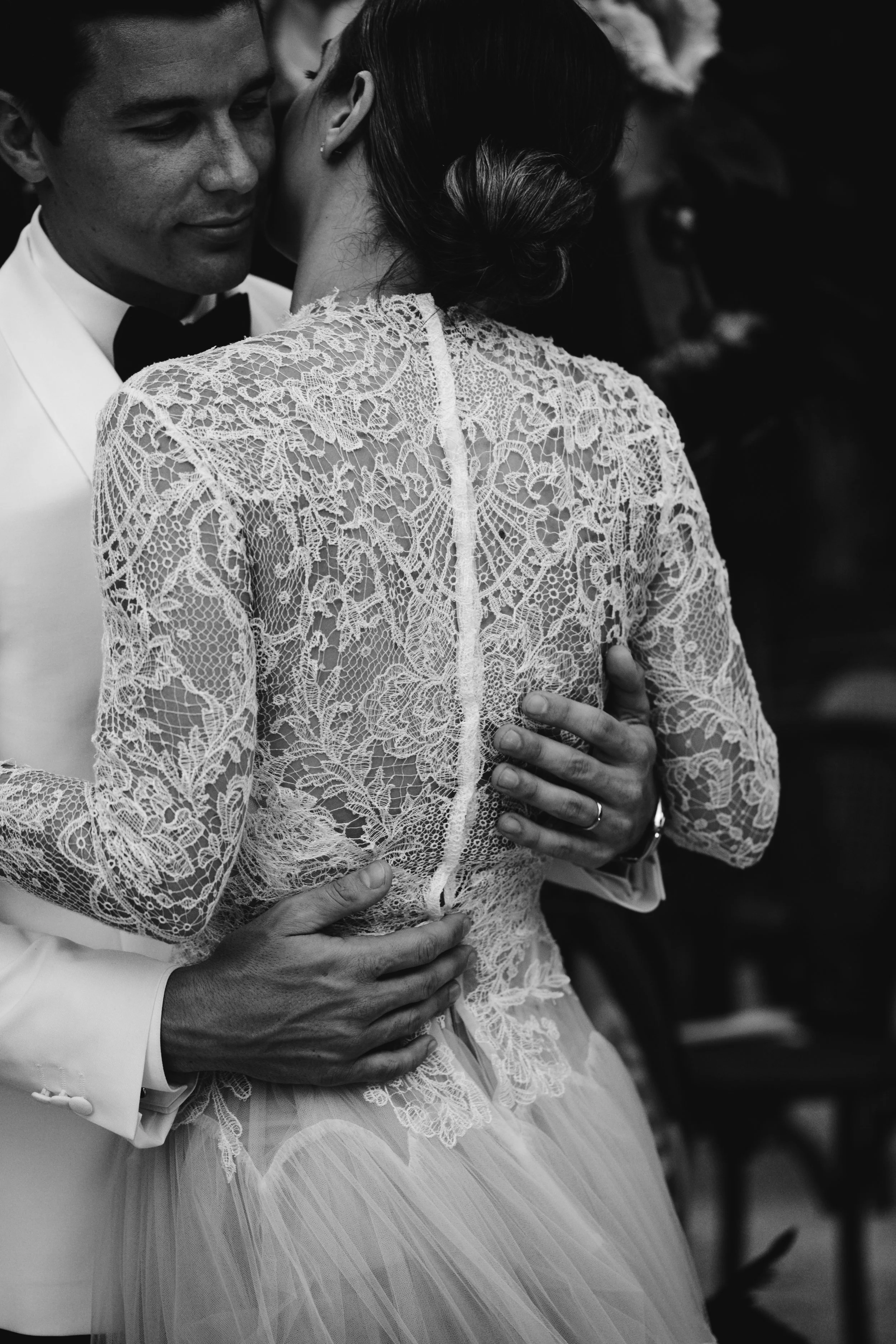 Pareja de novios en un abrazo romántico en su boda, la novia lleva vestido de encaje y el novio traje blanco, en negro y blanco.