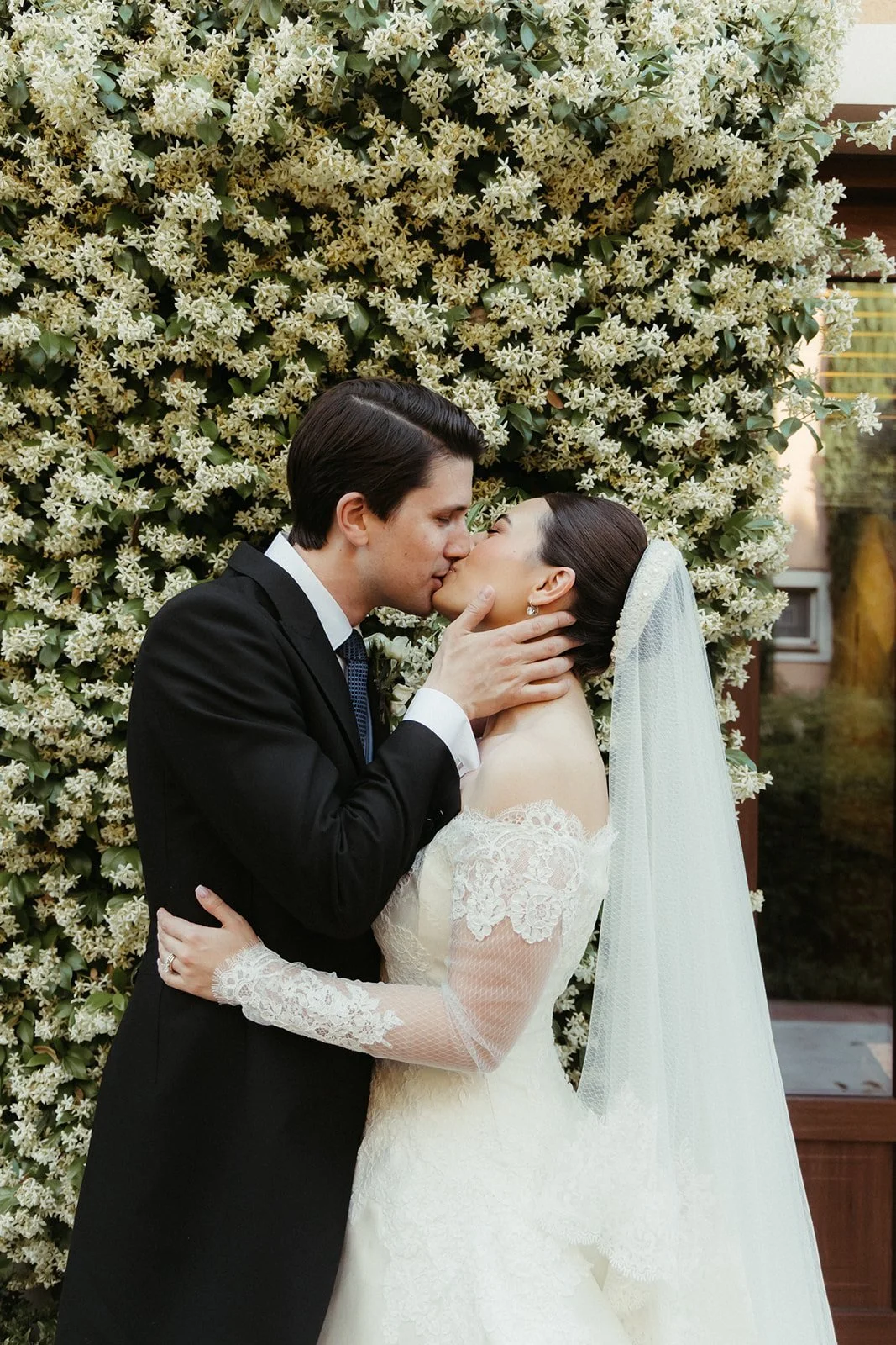 Los novios abrazados frente al muro de jazmín