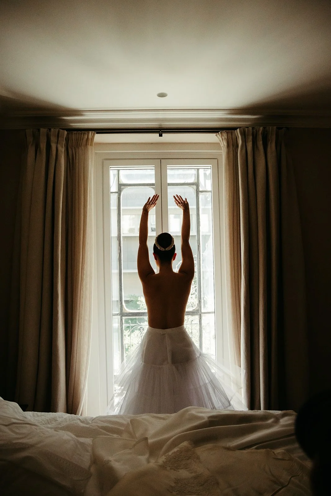 Silhouette of the bride in her gown against the hotel window