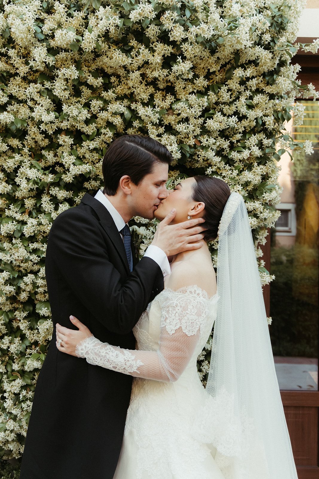 The couple embracing in front of the jasmine wall