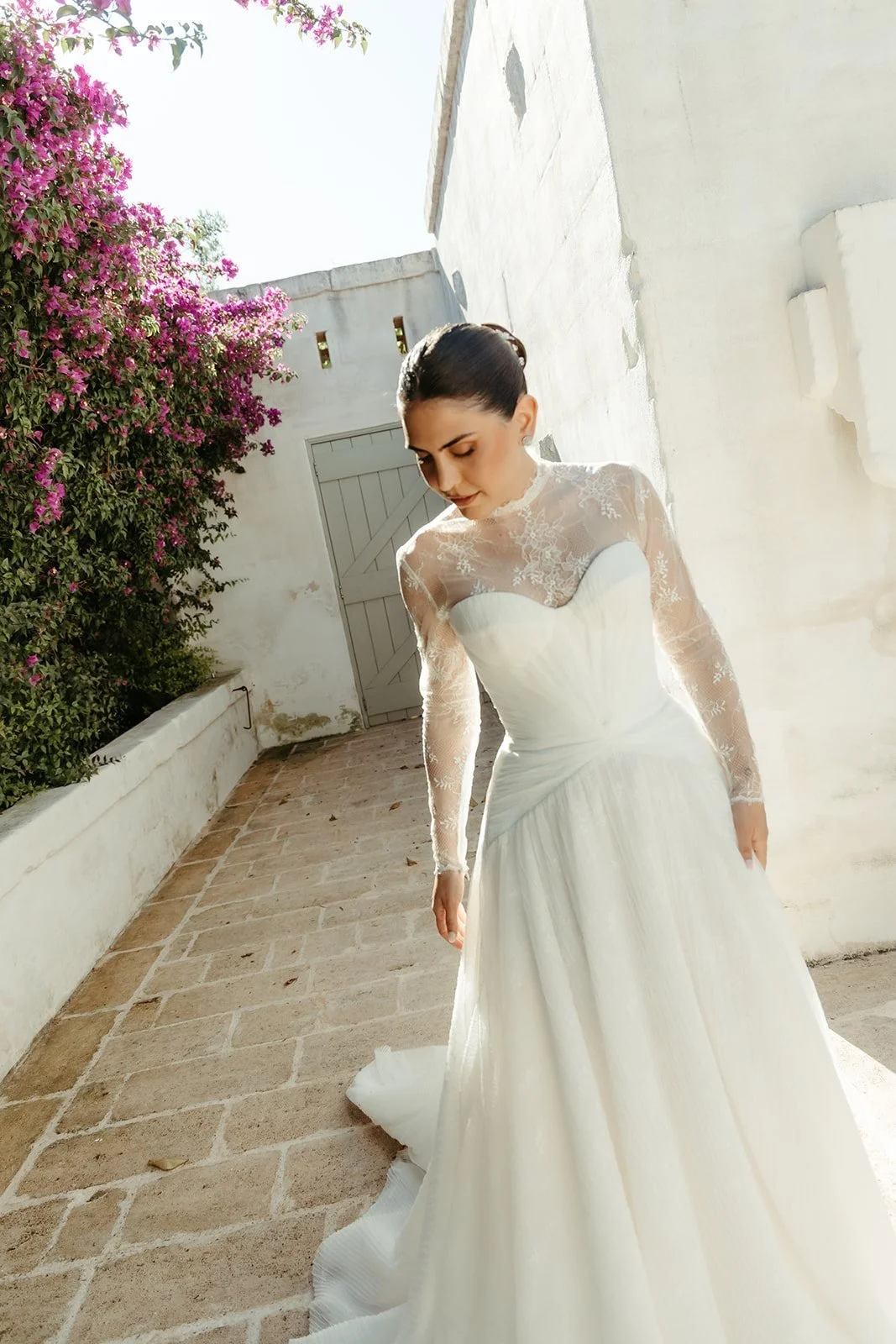 Valentina con su vestido en un callejón blanco con buganvilla en la masseria