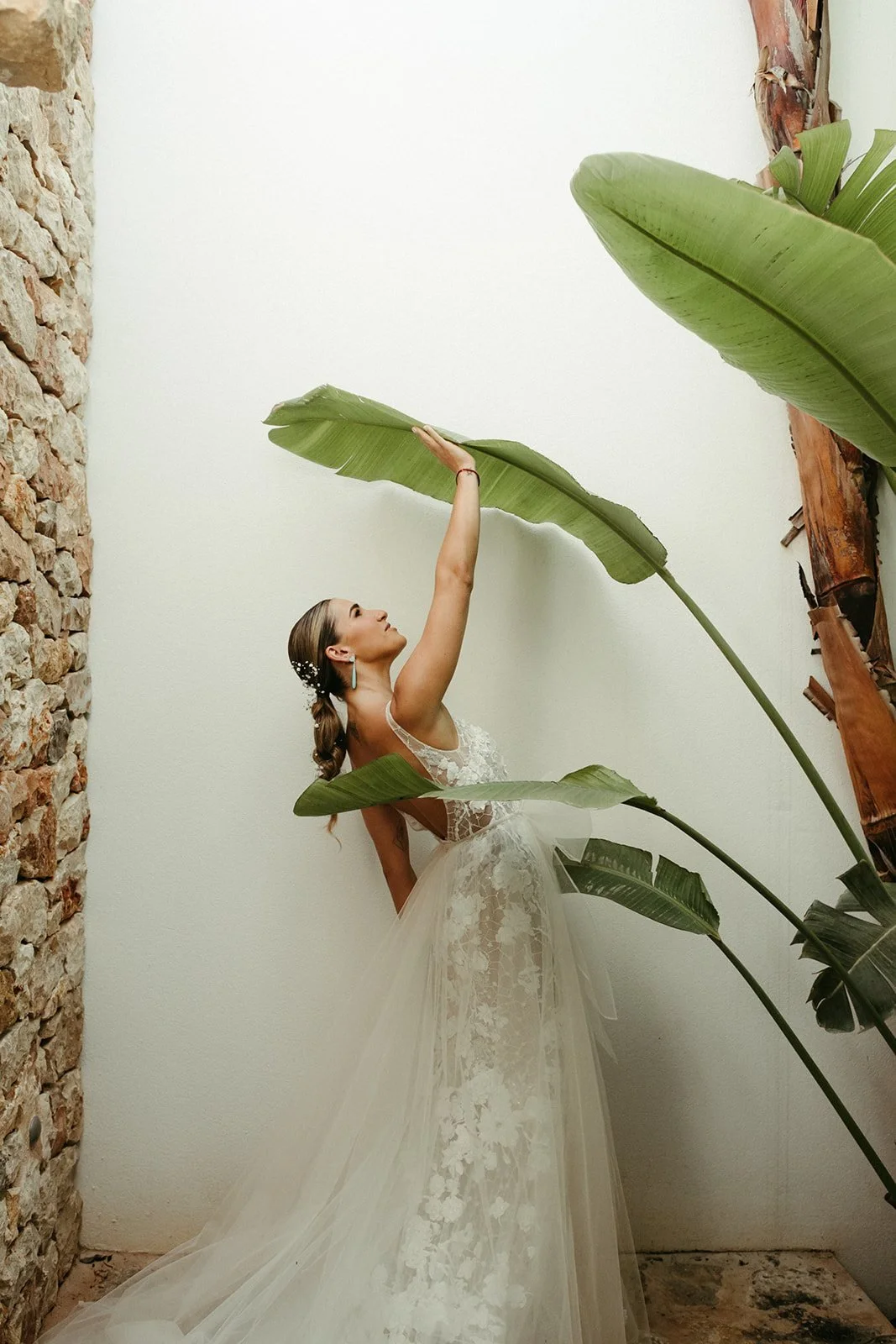 La novia junto a las hojas de platanera en una pared blanca de la villa