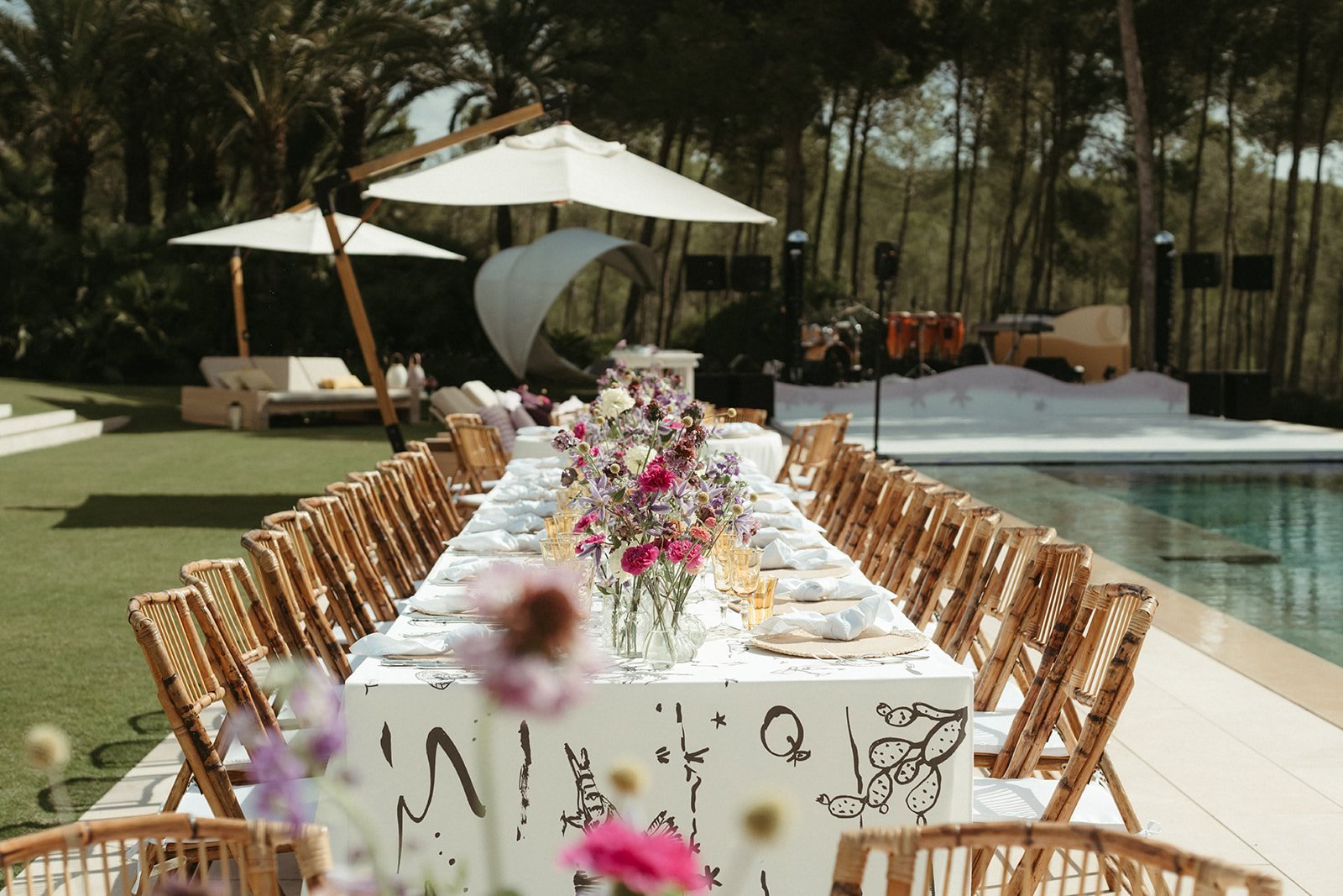 Mesa larga junto a la piscina de la villa, con flores y mantel ilustrado