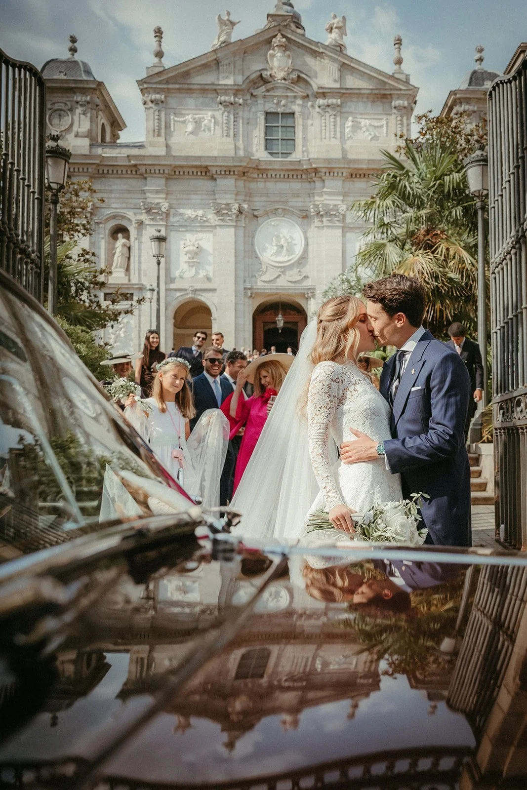 Los novios se besan reflejados en el capó del coche frente a Santa Bárbara
