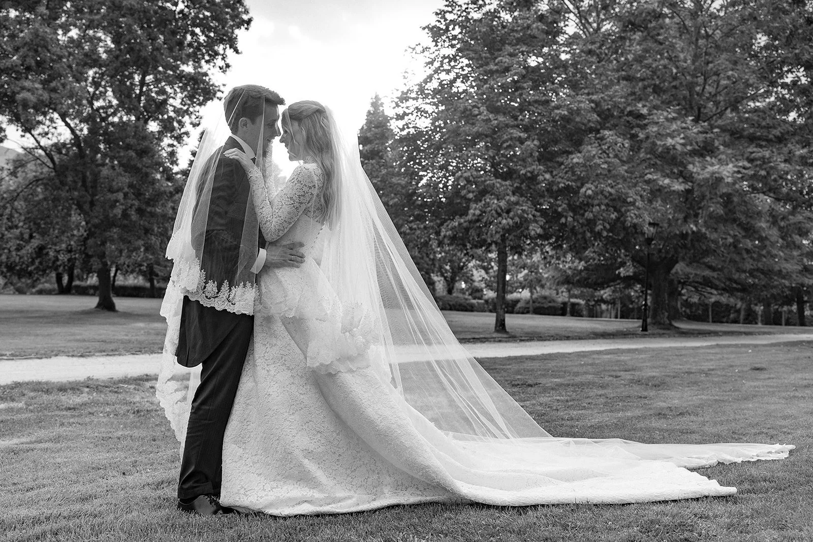 Beso de los novios con el velo extendido sobre el césped, en blanco y negro