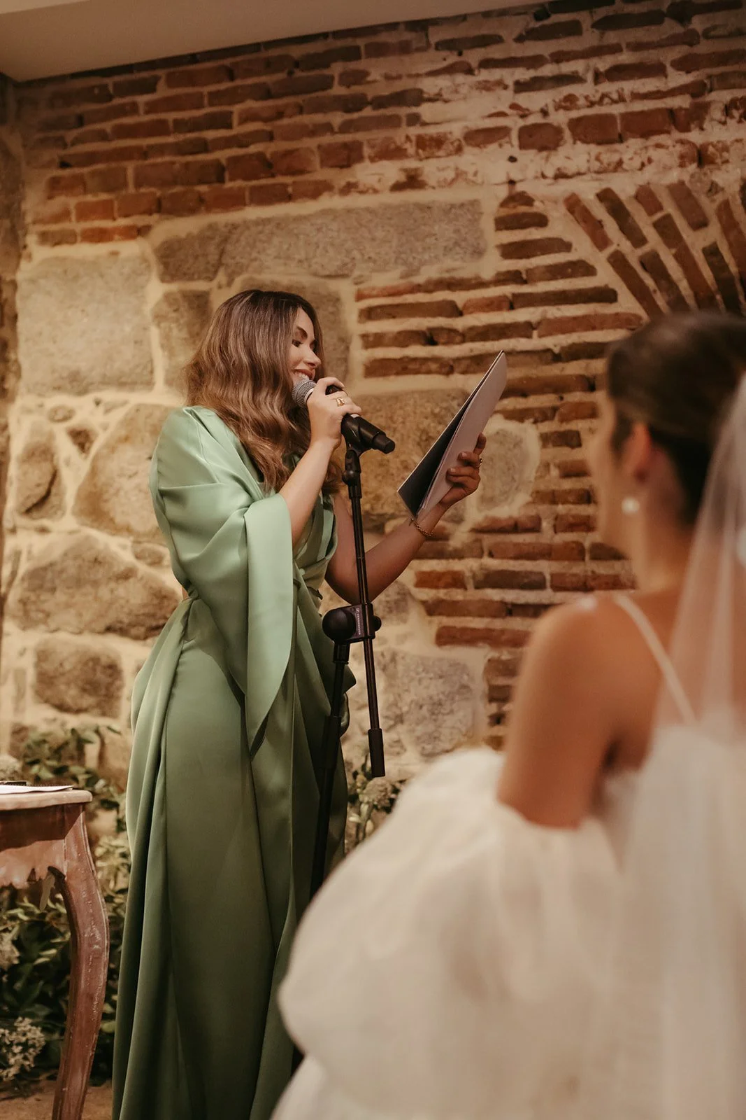 Una mujer canta al micrófono frente a la novia en la ceremonia de Paola y Daniel, en El Escorial