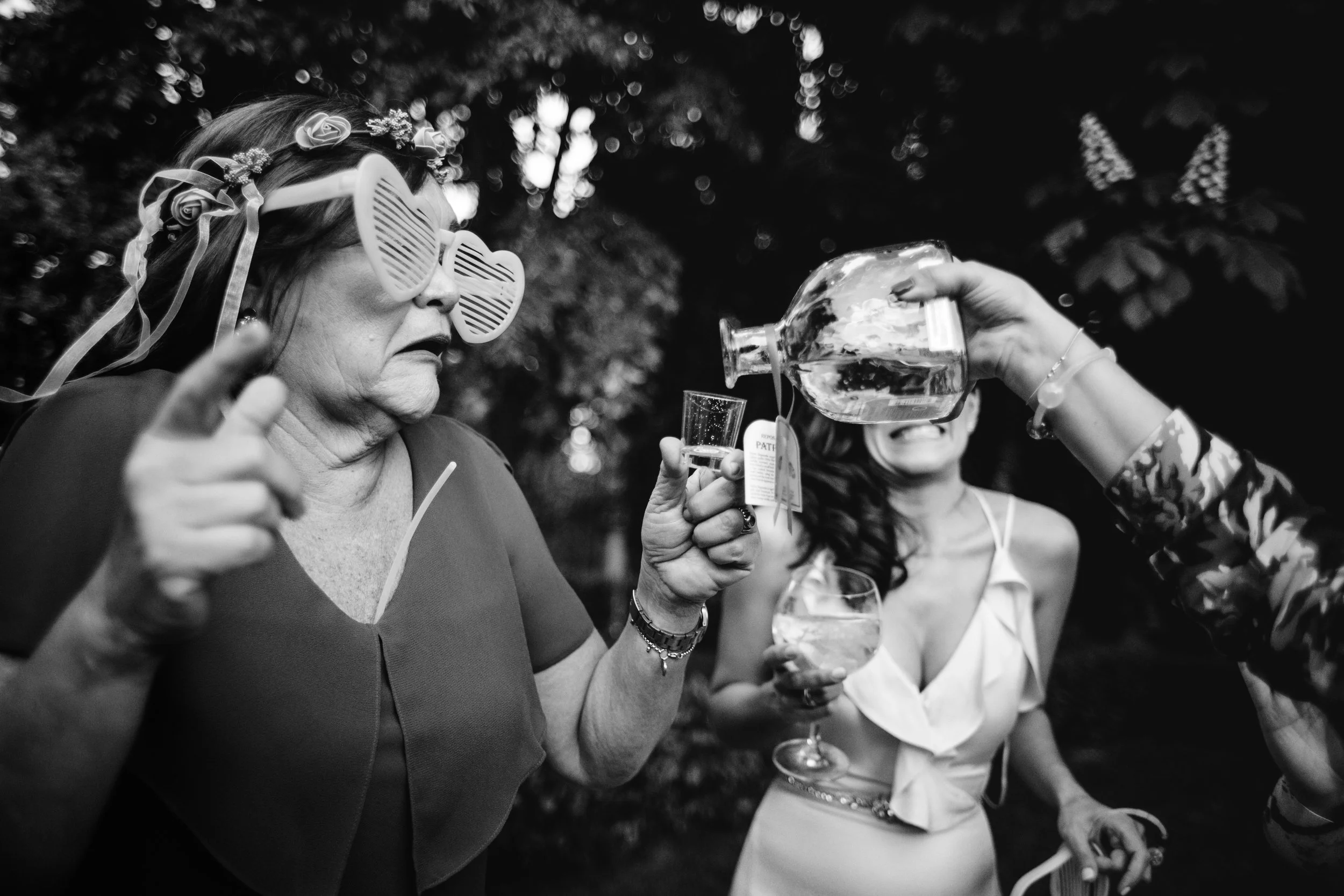 Mujeres en una celebración o fiesta, una de ellas con gafas de cerdo y corona de flores, sirviendo bebida a otra persona en un entorno exterior.