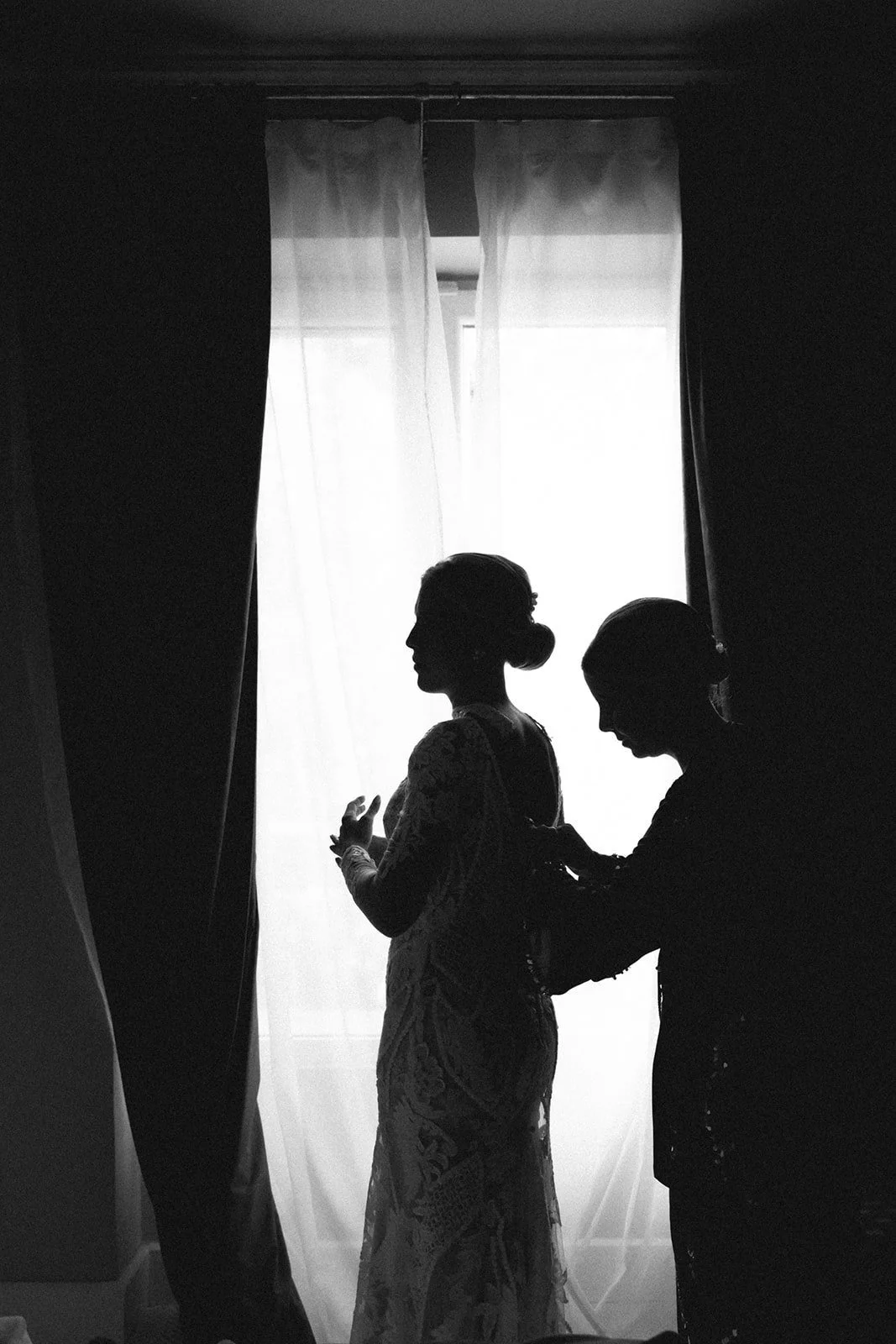 Silhouette of the bride being helped into her dress by a window before her wedding in Madrid