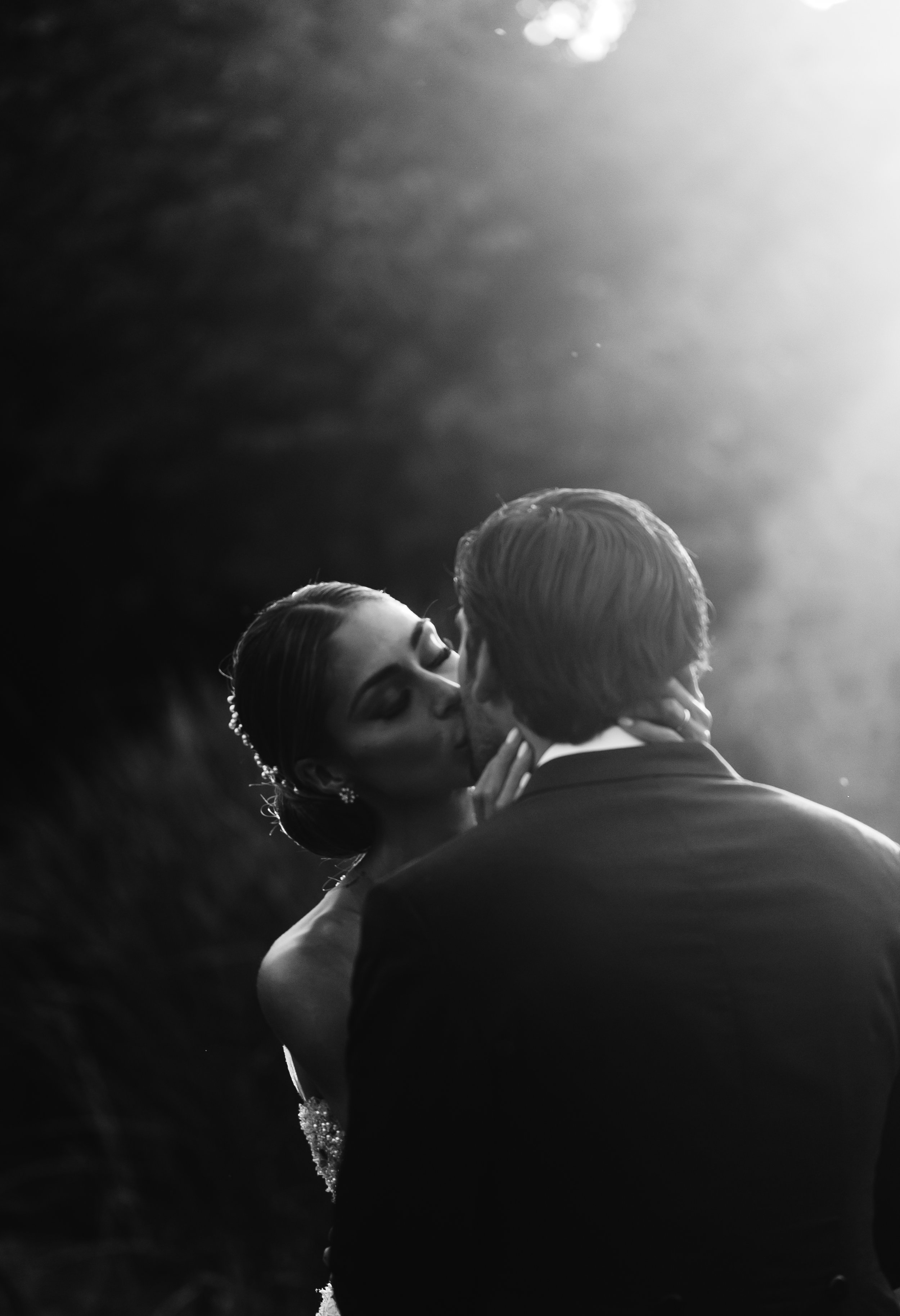 Pareja de recién casados compartiendo un beso en blanco y negro, en un ambiente romántico y elegante.