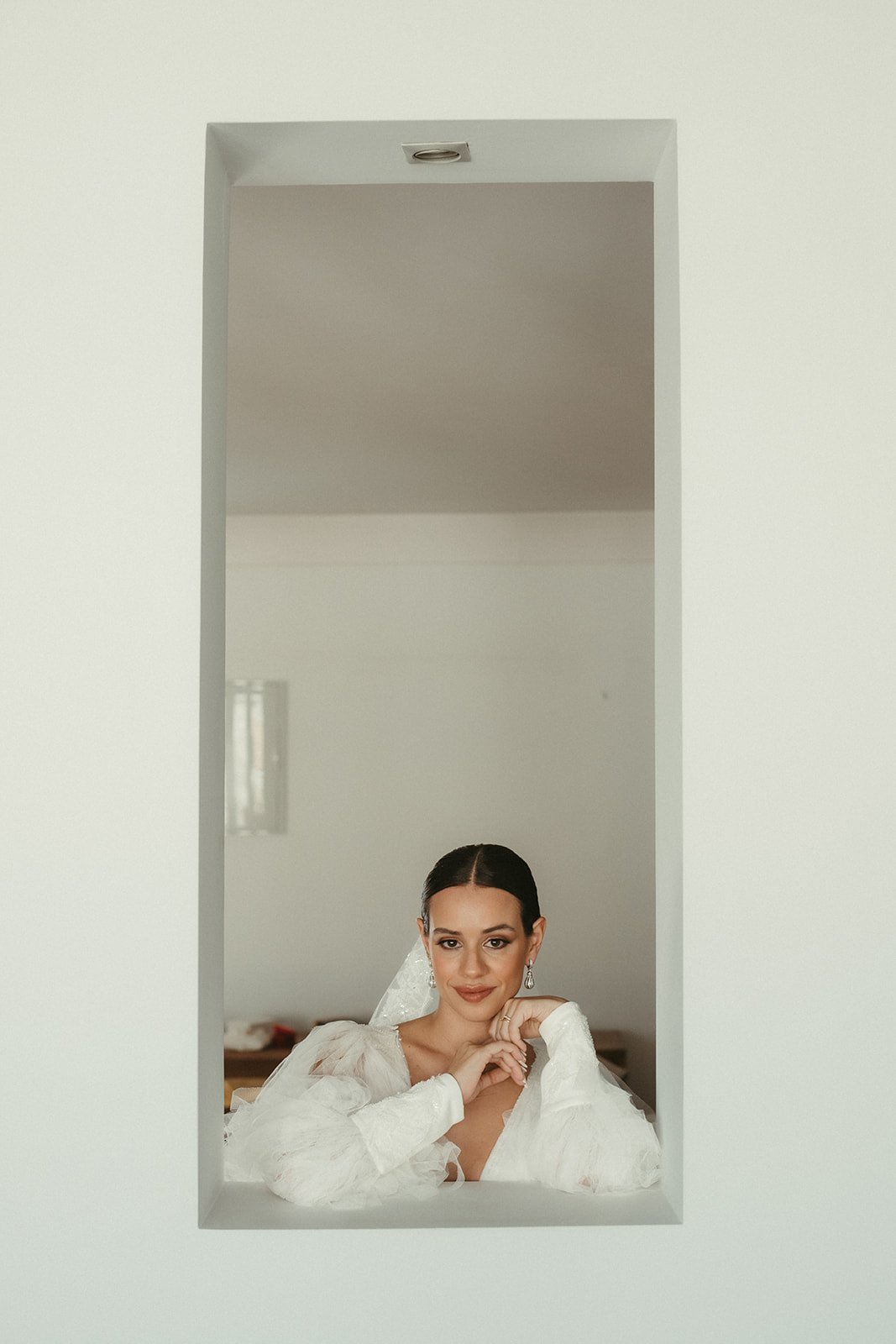 Bride smiling from a white window niche while getting ready for her wedding in Madrid