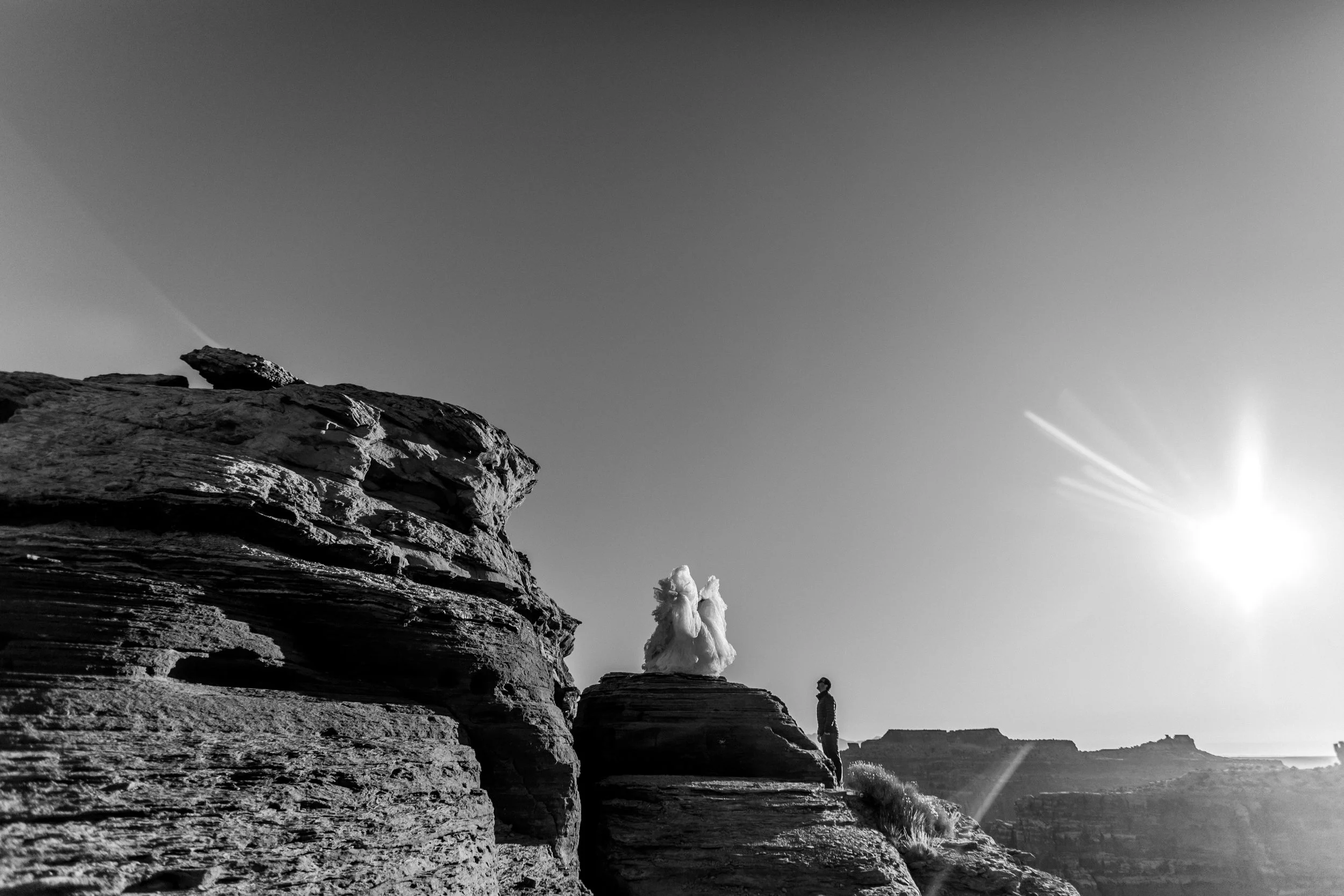 Un paisaje de formaciones rocosas en un entorno desértico con un cielo despejado y el sol brillante en el horizonte.
