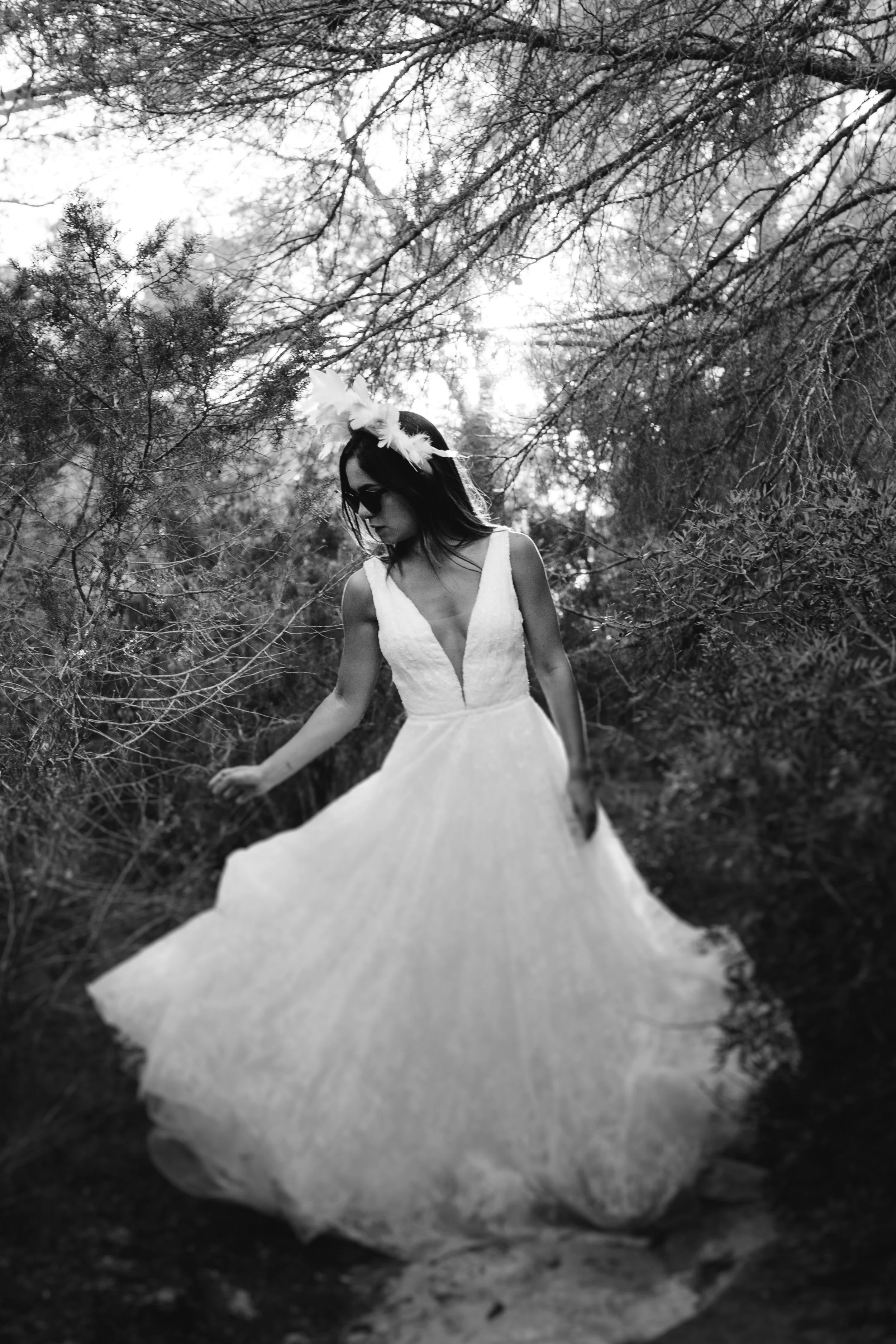 Mujer con vestido blanco largo y diadema con plumas en un bosque.