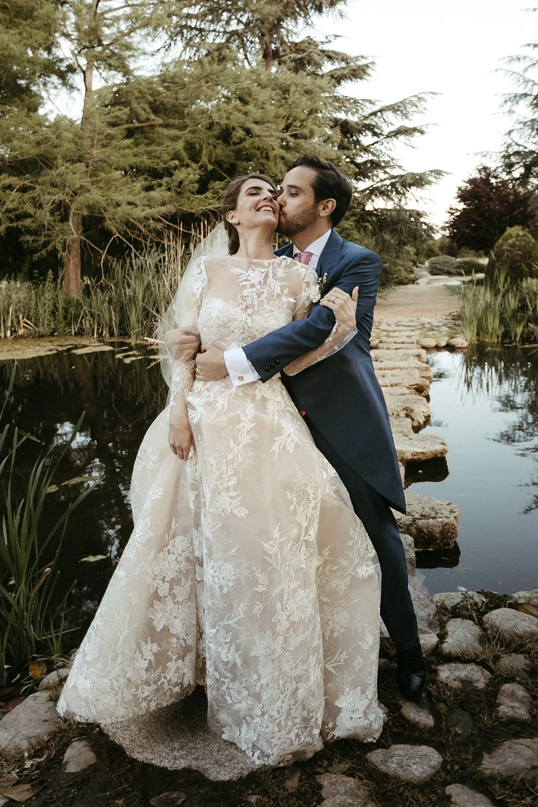 Groom kissing the bride on the stepping stones of a garden pond at a wedding estate near El Escorial, Madrid