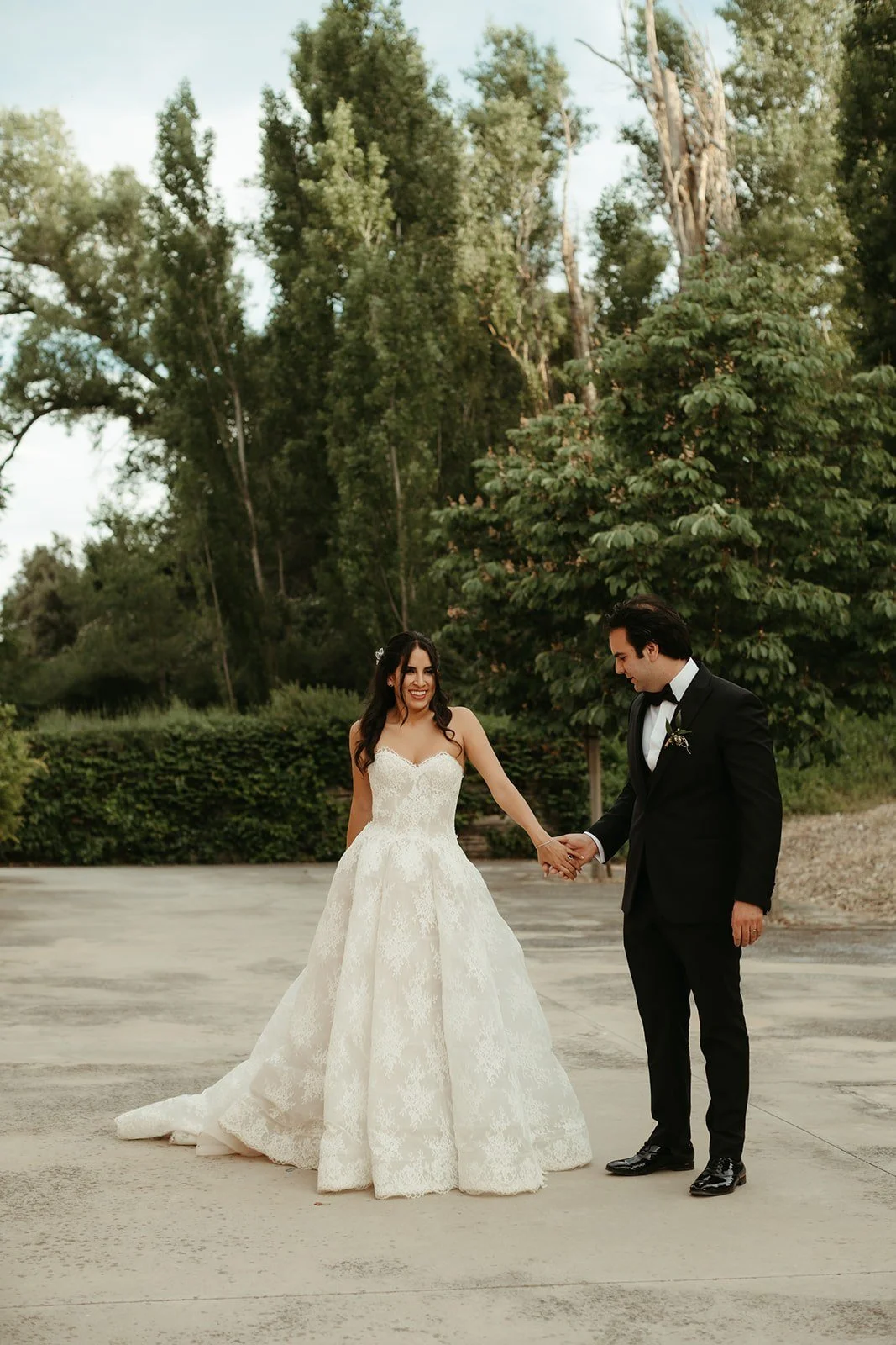Bride and groom holding hands under tall poplar trees on their wedding day in Madrid