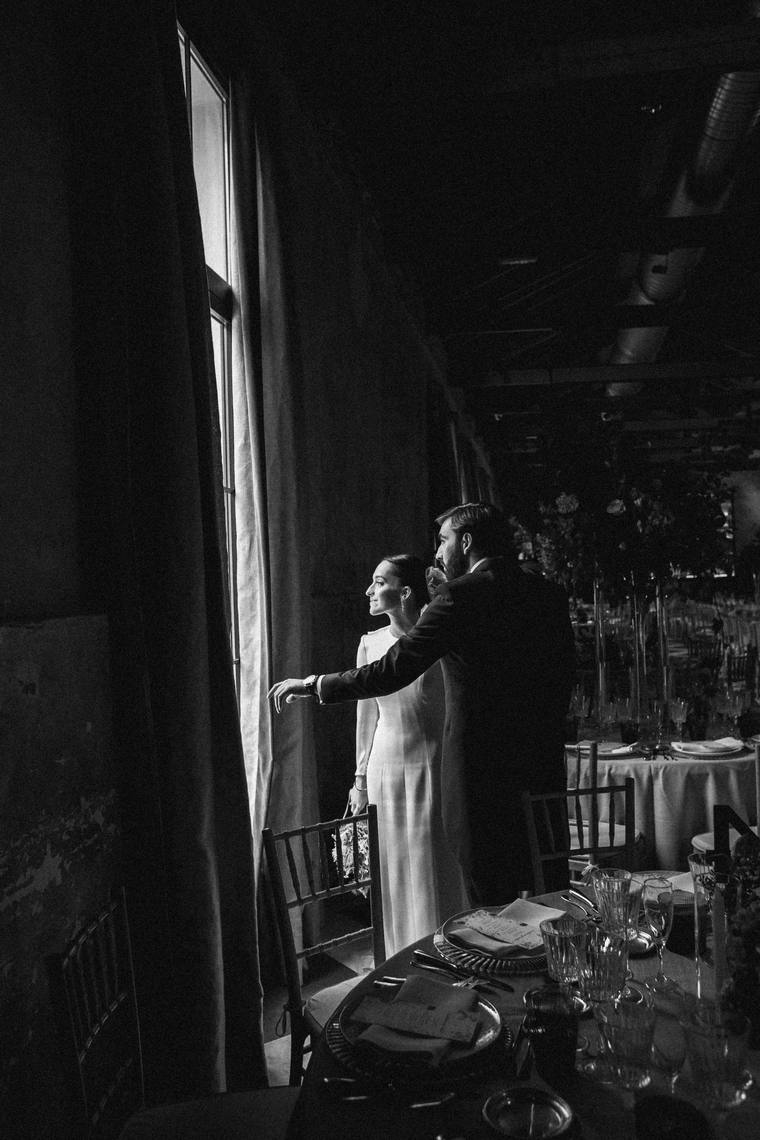 Pareja en una boda, de pie junto a la ventana en un lugar elegante.