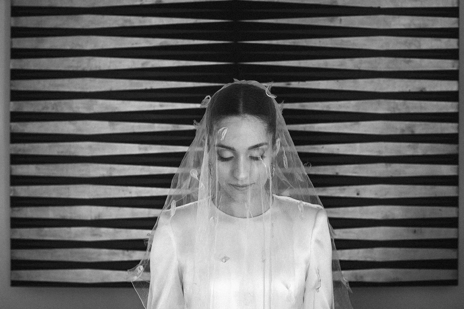 Black and white portrait of the bride in a high-neck dress and long veil before her Madrid wedding