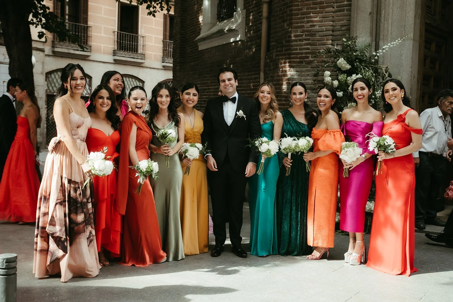 Bridesmaids in colourful gowns with the groom outside the church of San Antonio de los Alemanes, Madrid