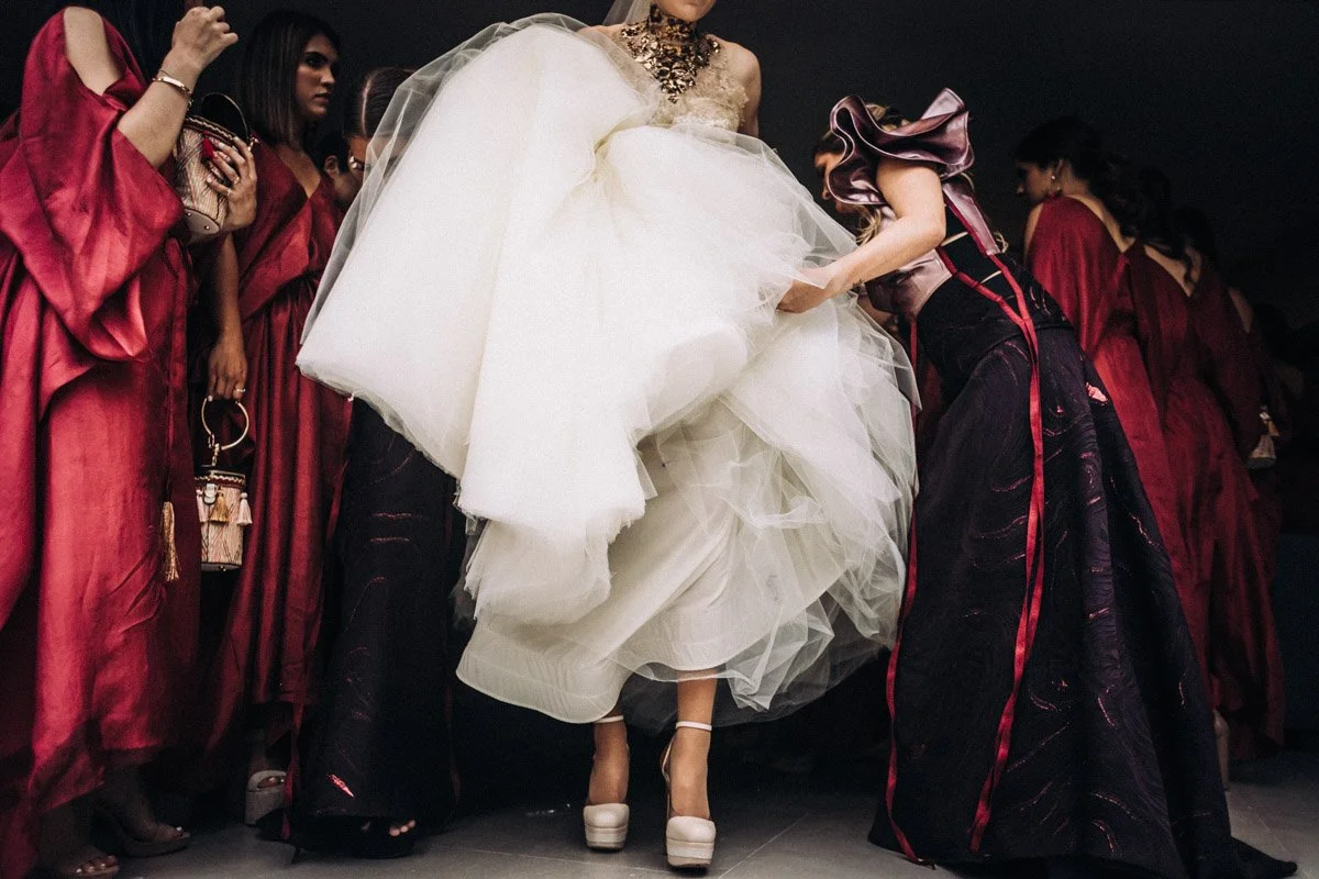 Mujeres en una pasarela, con varias vestidas con prendas de color rojo y una mujer en el centro lleva un vestido de novia blanco.
