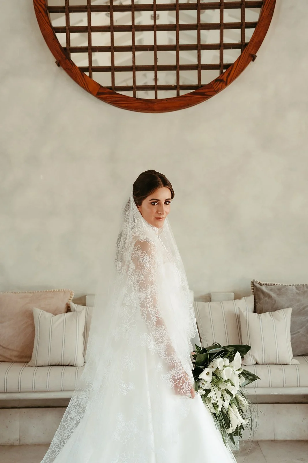 Bride in a long lace veil holding white calla lilies before her wedding in Madrid