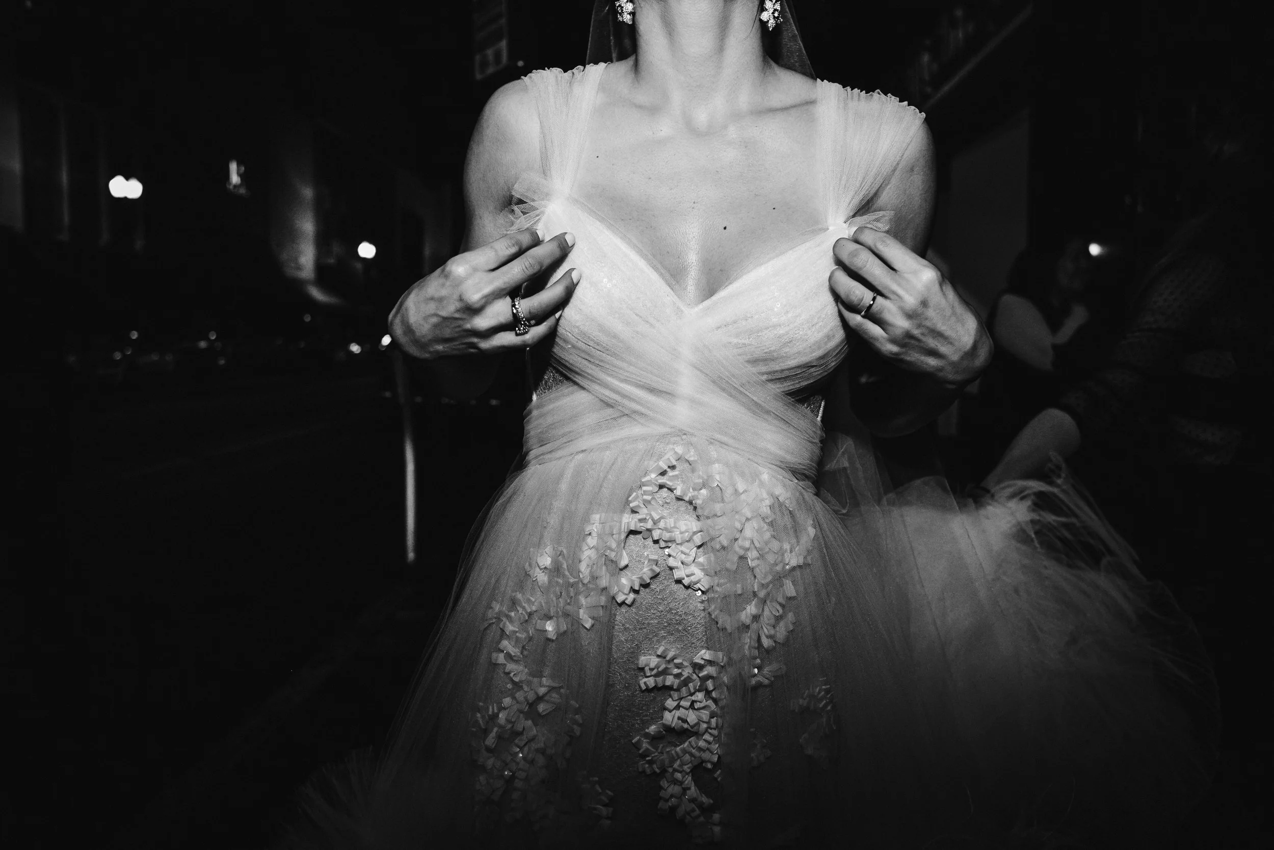 Mujer con vestido de novia ajustado y detalles de encaje, en un ambiente oscuro.